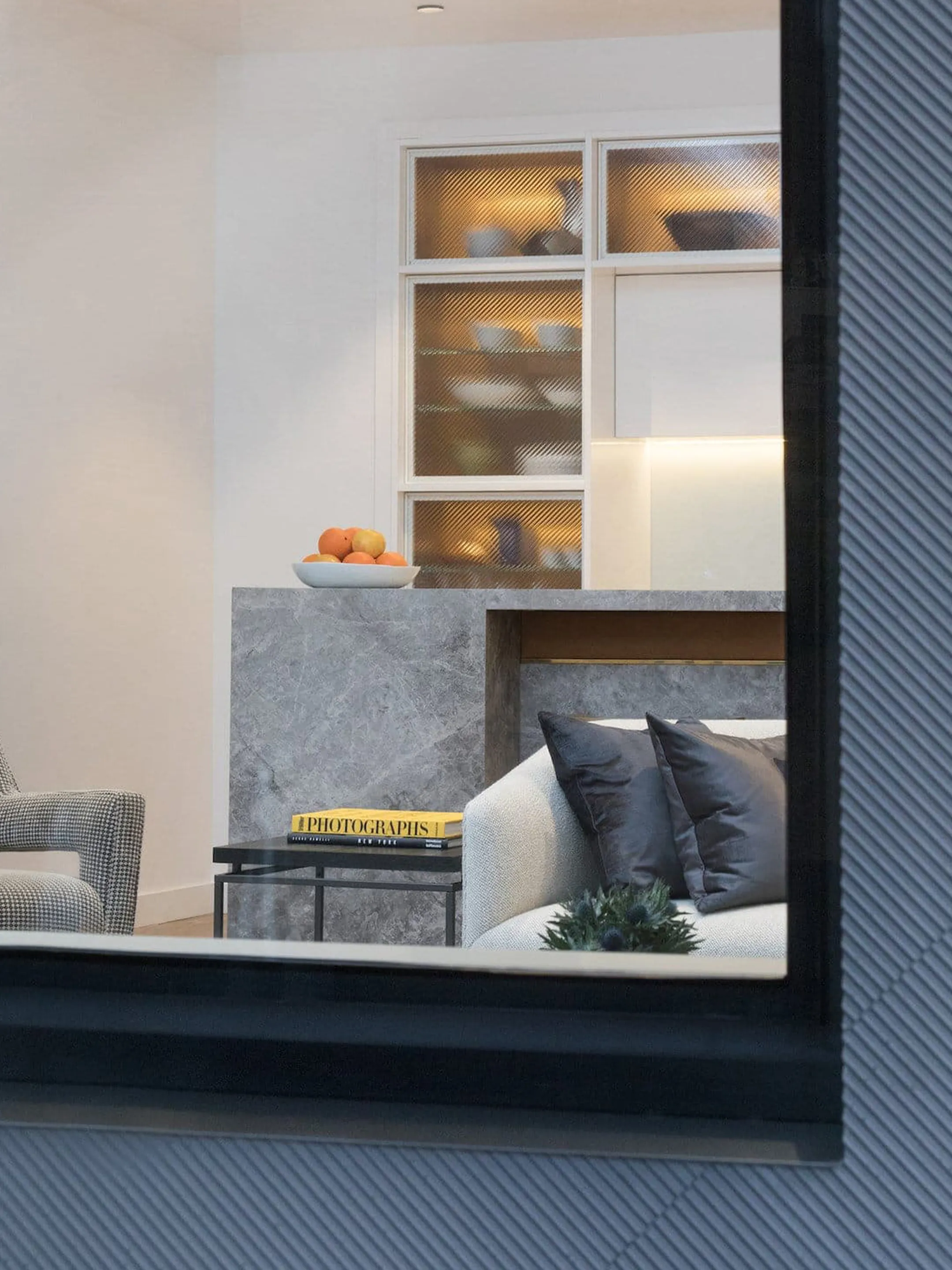 View through a window into a living area with a pale sofa, gray counter, and illuminated cabinets.