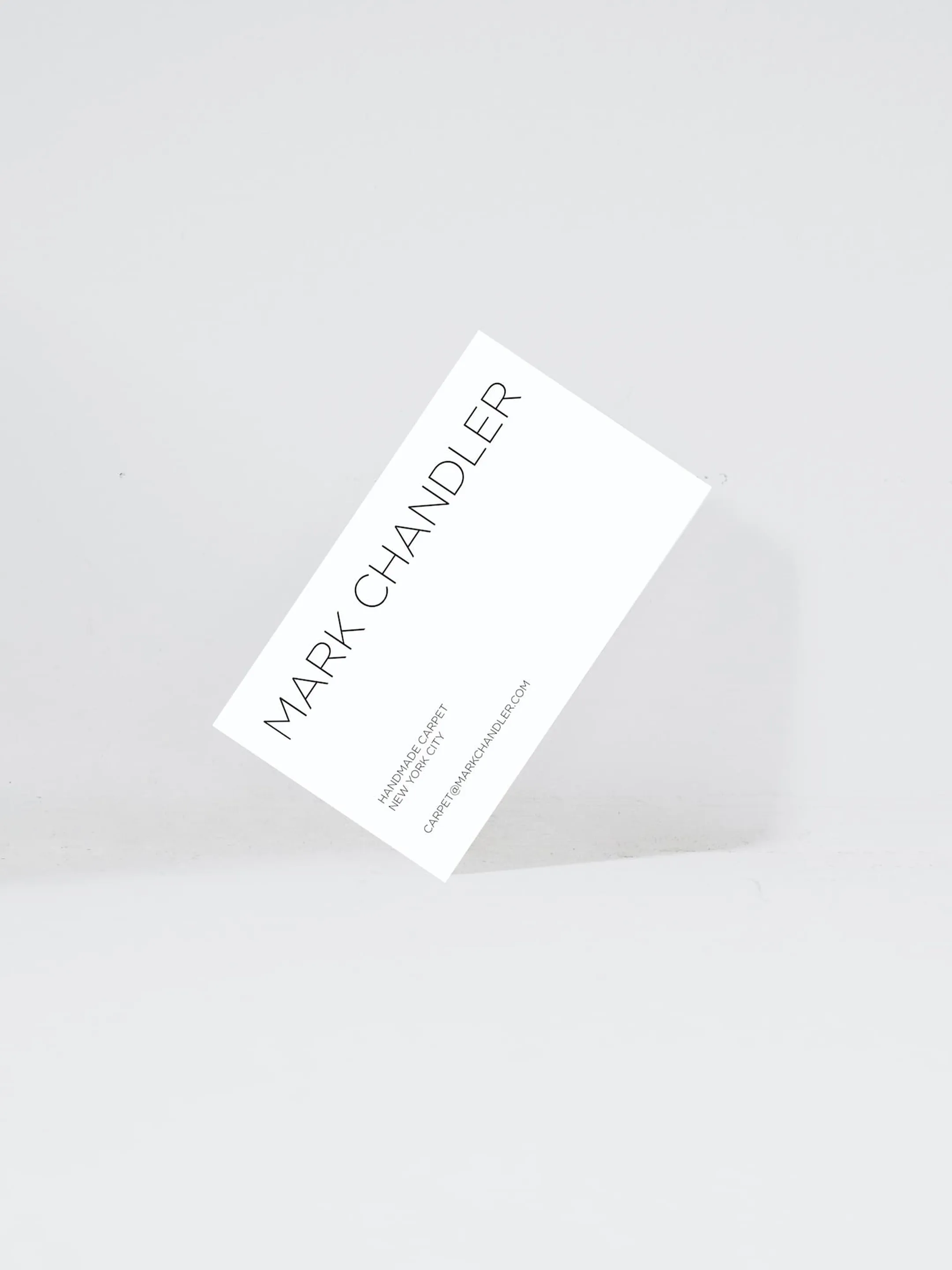 White Mark Chandler business card tilted against a pale gray background.