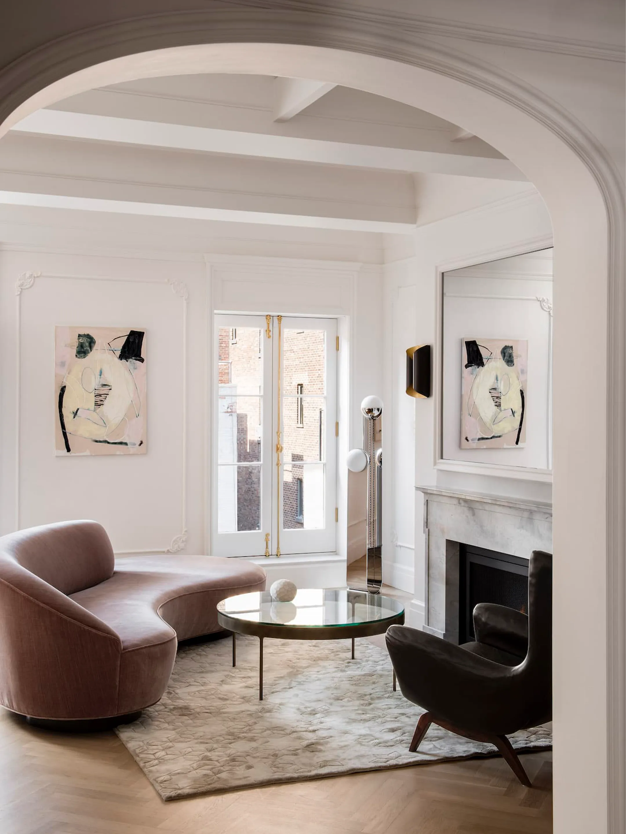 Arched doorway framing a living room with a curved mauve sofa, glass table, and fireplace.