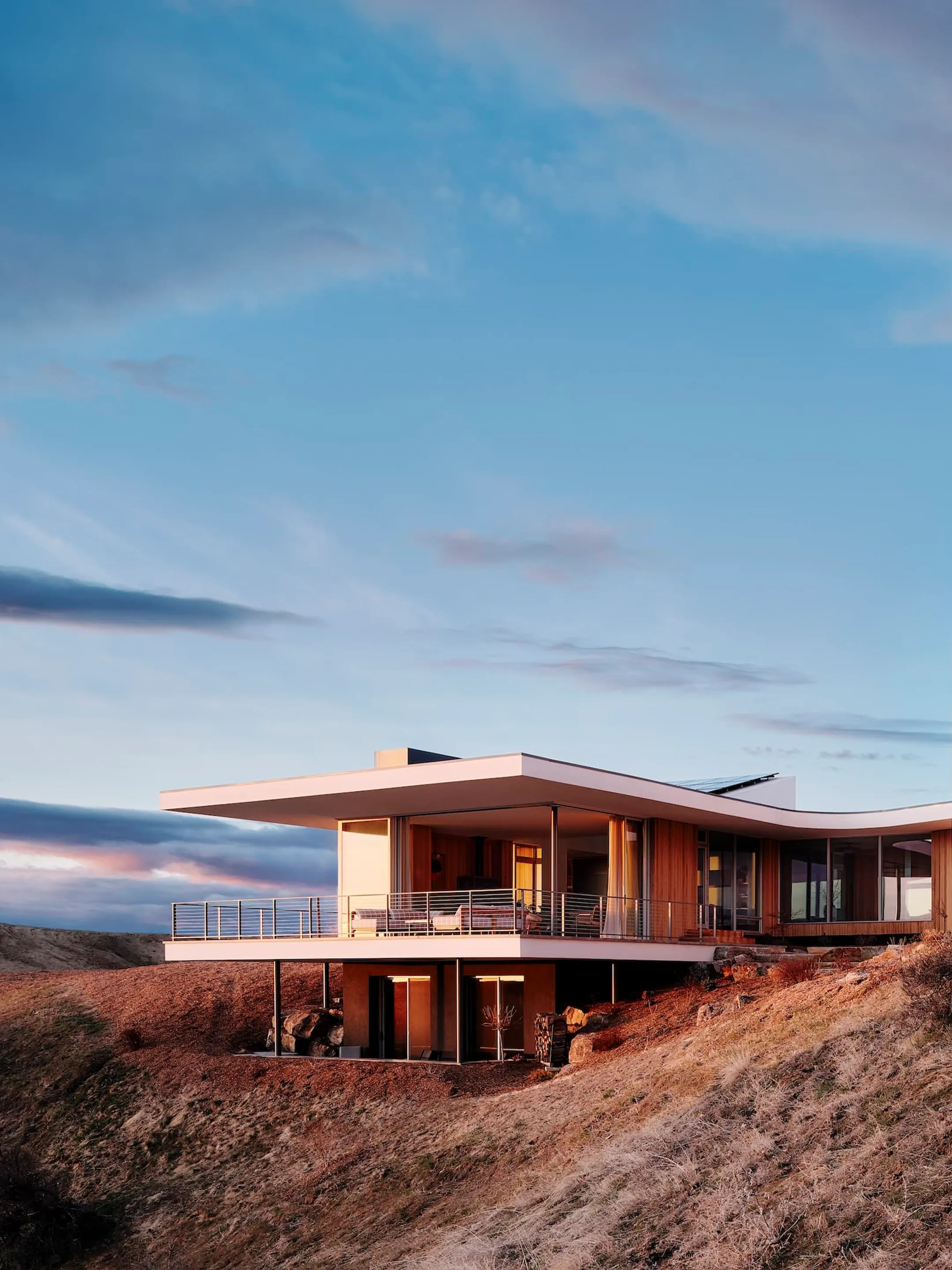 Modern house with a broad overhanging roof on a dry hillside at dusk.