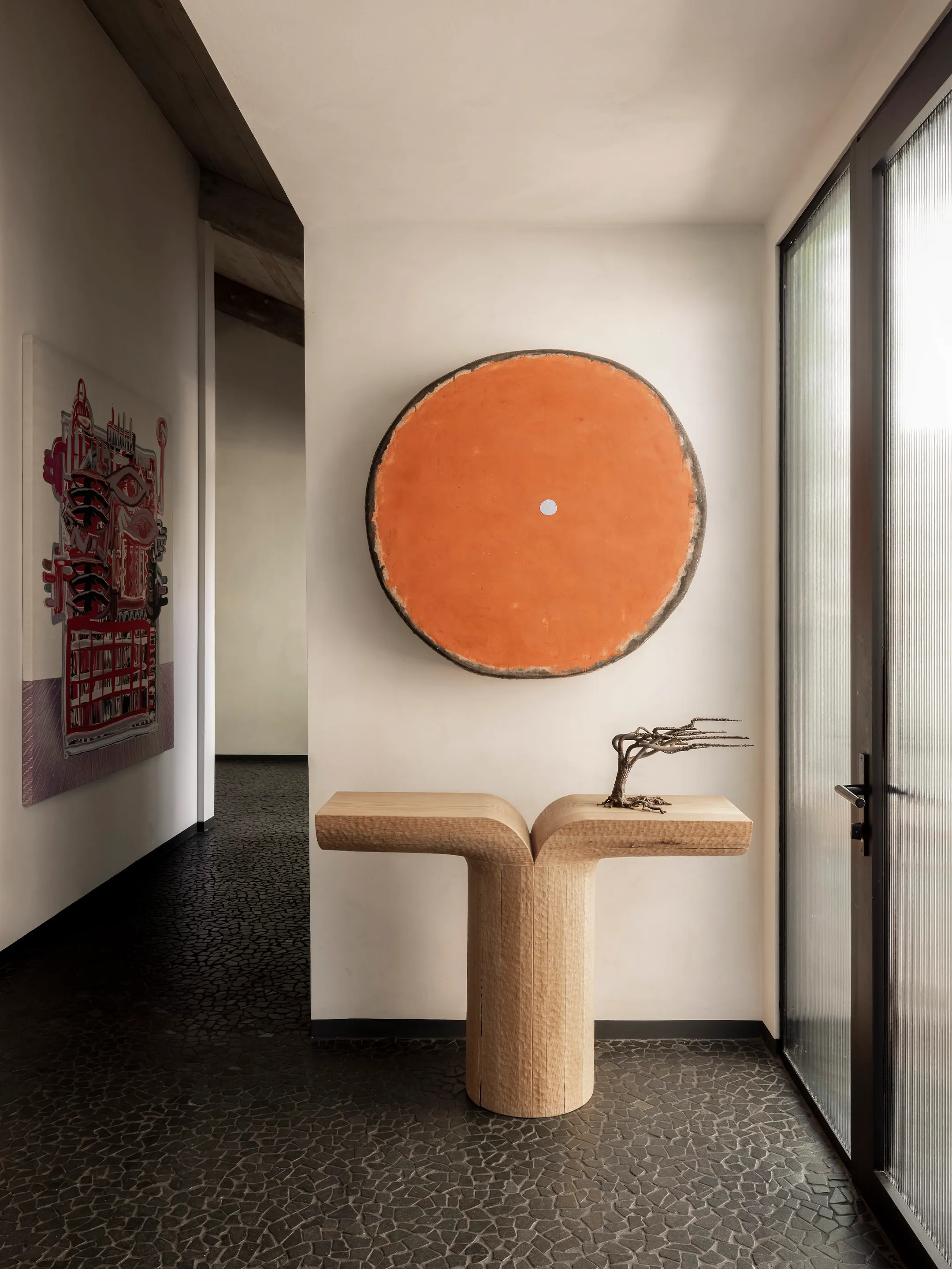 Entryway with a sculptural console beneath a large orange circular artwork.