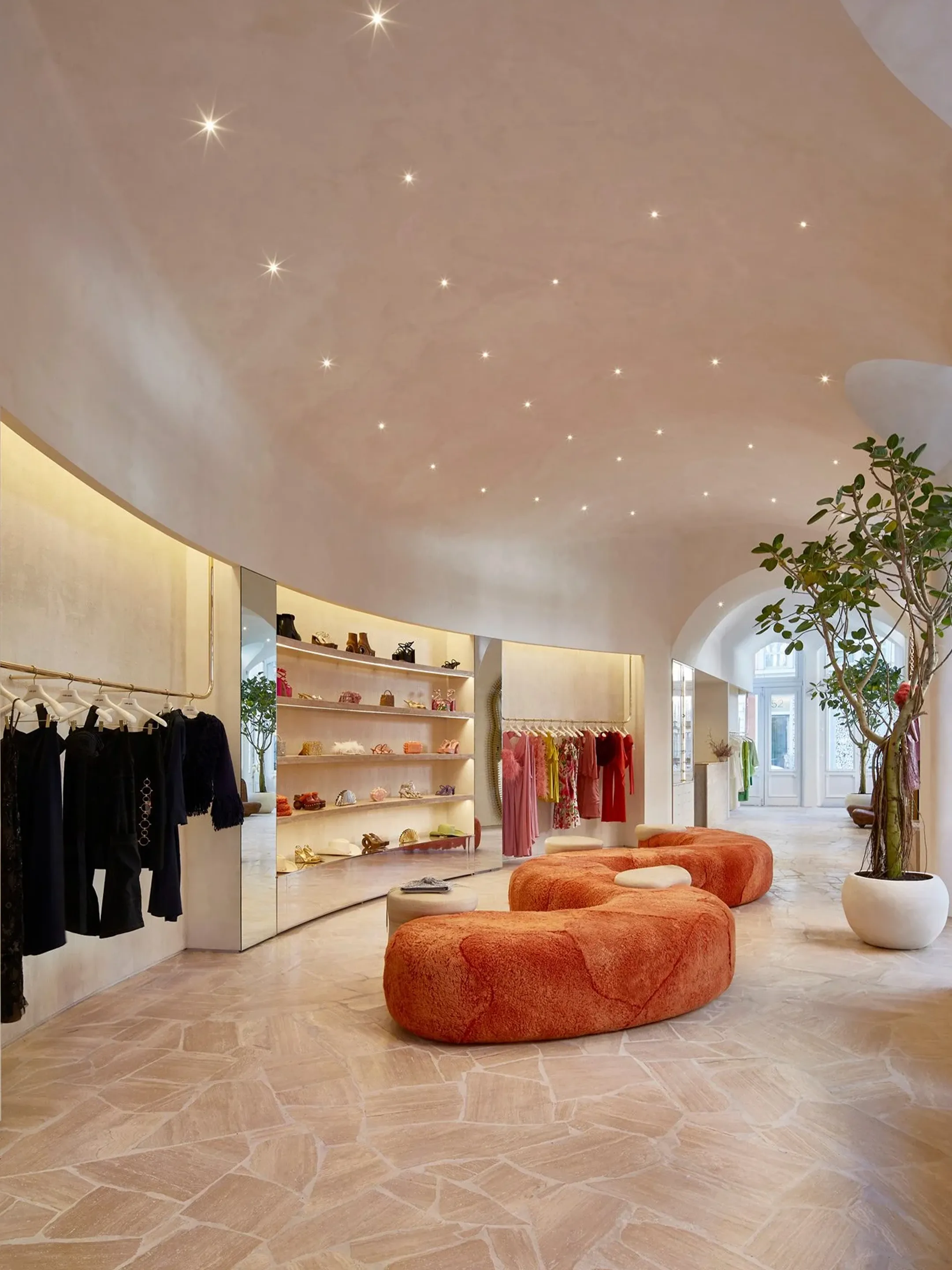 Clothing boutique with curved orange seating, illuminated shelves, and a sweeping ceiling.