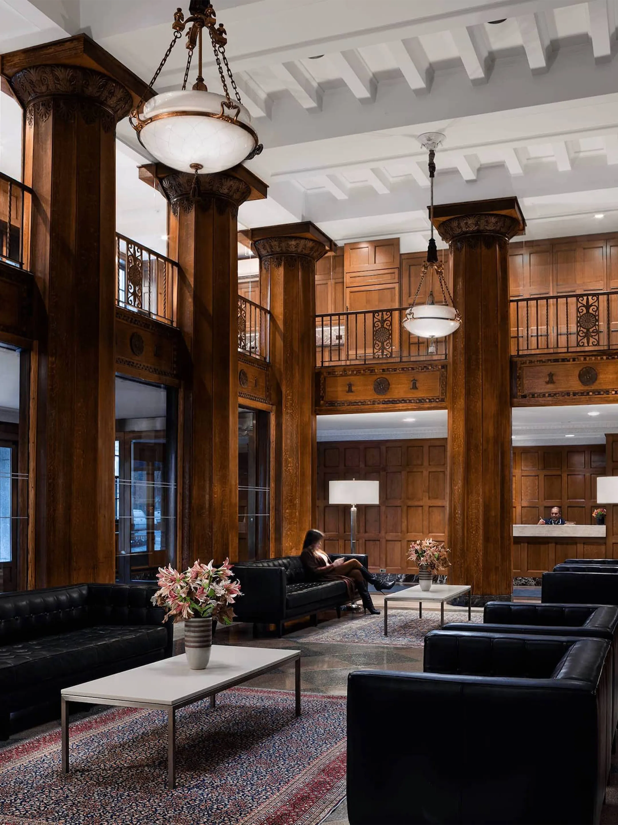 Double-height lounge with wood-paneled columns, pendant lights, and black sofas.