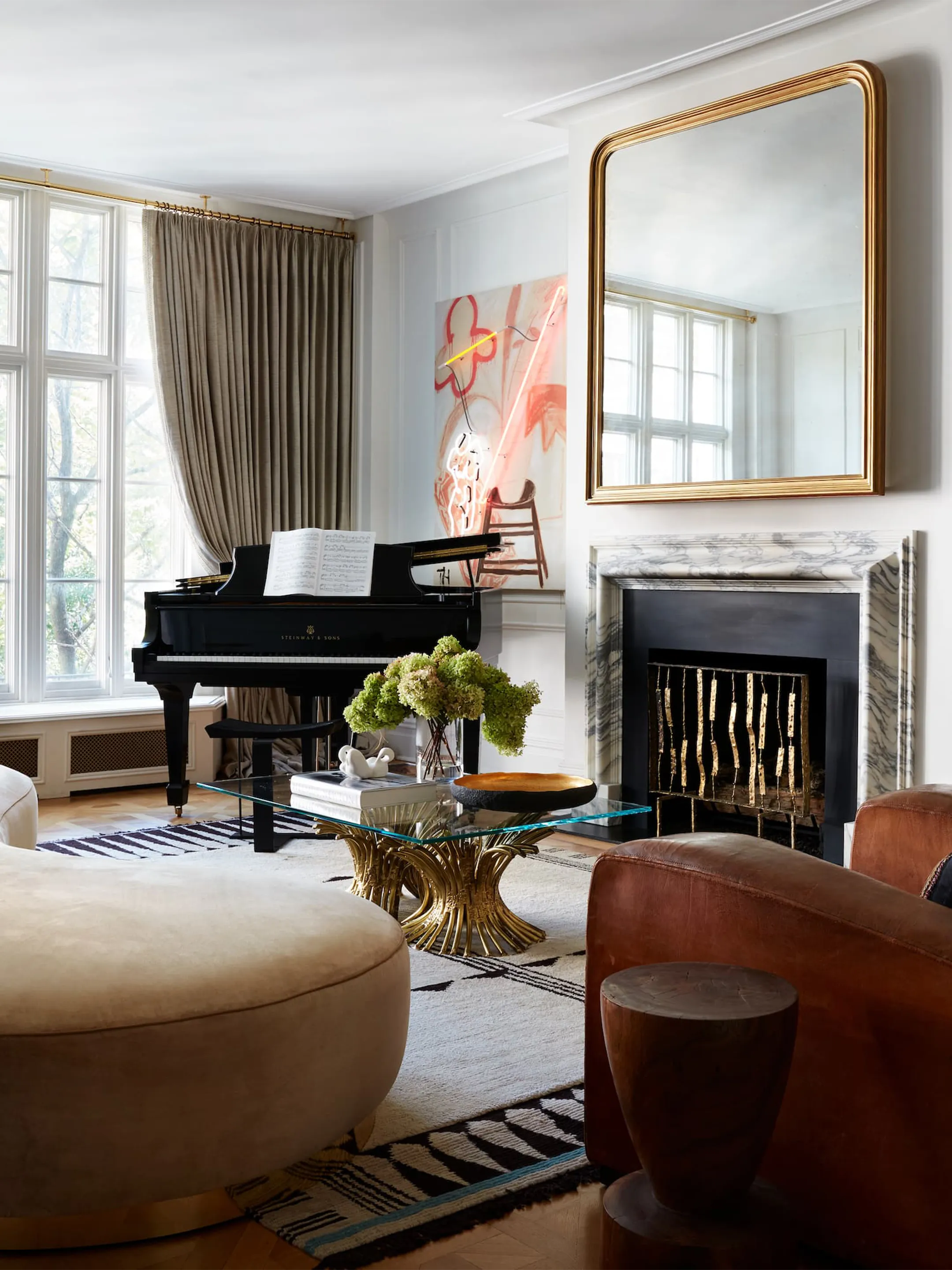 Living room with a grand piano, fireplace, gold-framed mirror, and curved seating.