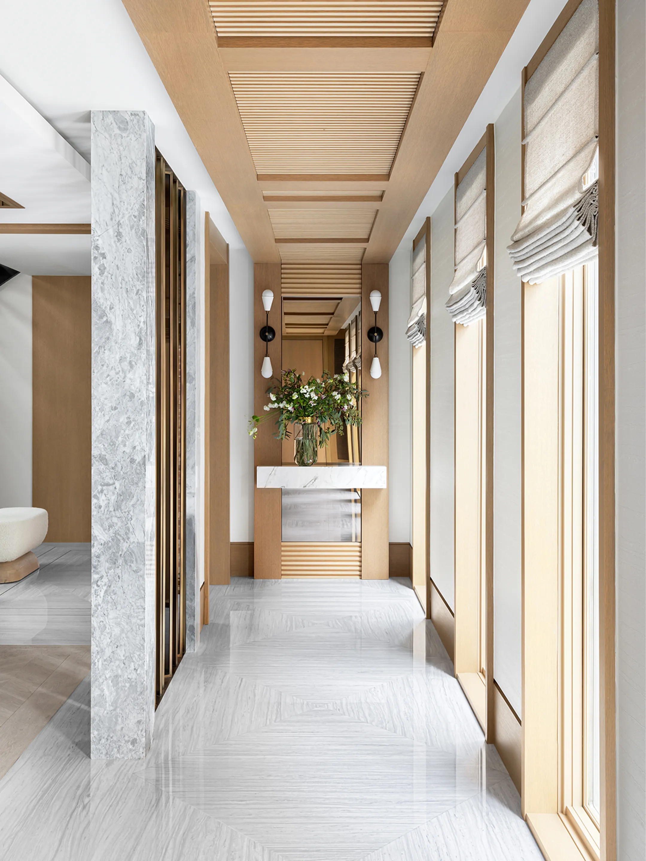 Bright corridor with tall windows, wood ceiling panels, and pale stone flooring.
