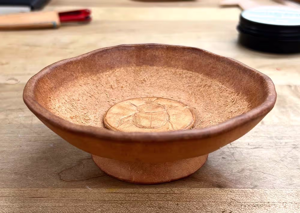 A leather jewelry dish with a beetle carved into the middle.