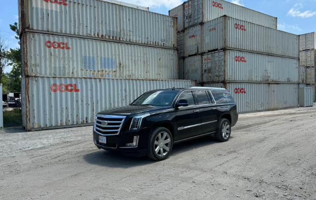Luxury black Cadillac Escalade SUV parked in front of stacked shipping containers, showcasing North End Shuttle’s premium fleet for transportation in Virginia Beach and Hampton Roads.