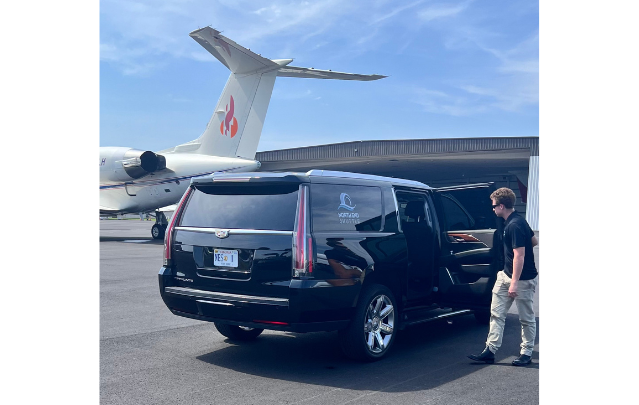 North End Shuttle’s luxury black Cadillac Escalade SUV parked at a private airport, offering VIP transportation services with a professional chauffeur ready to assist.