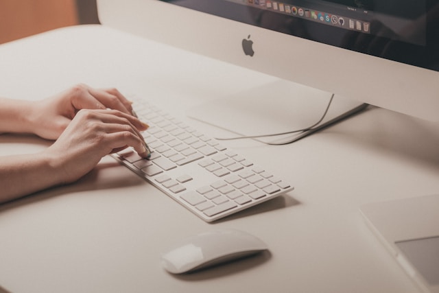 Close-up of a person typing on a white Apple Magic Keyboard and using a Magic Mouse on a clean, minimal desk, highlighting a Mac-native workflow.