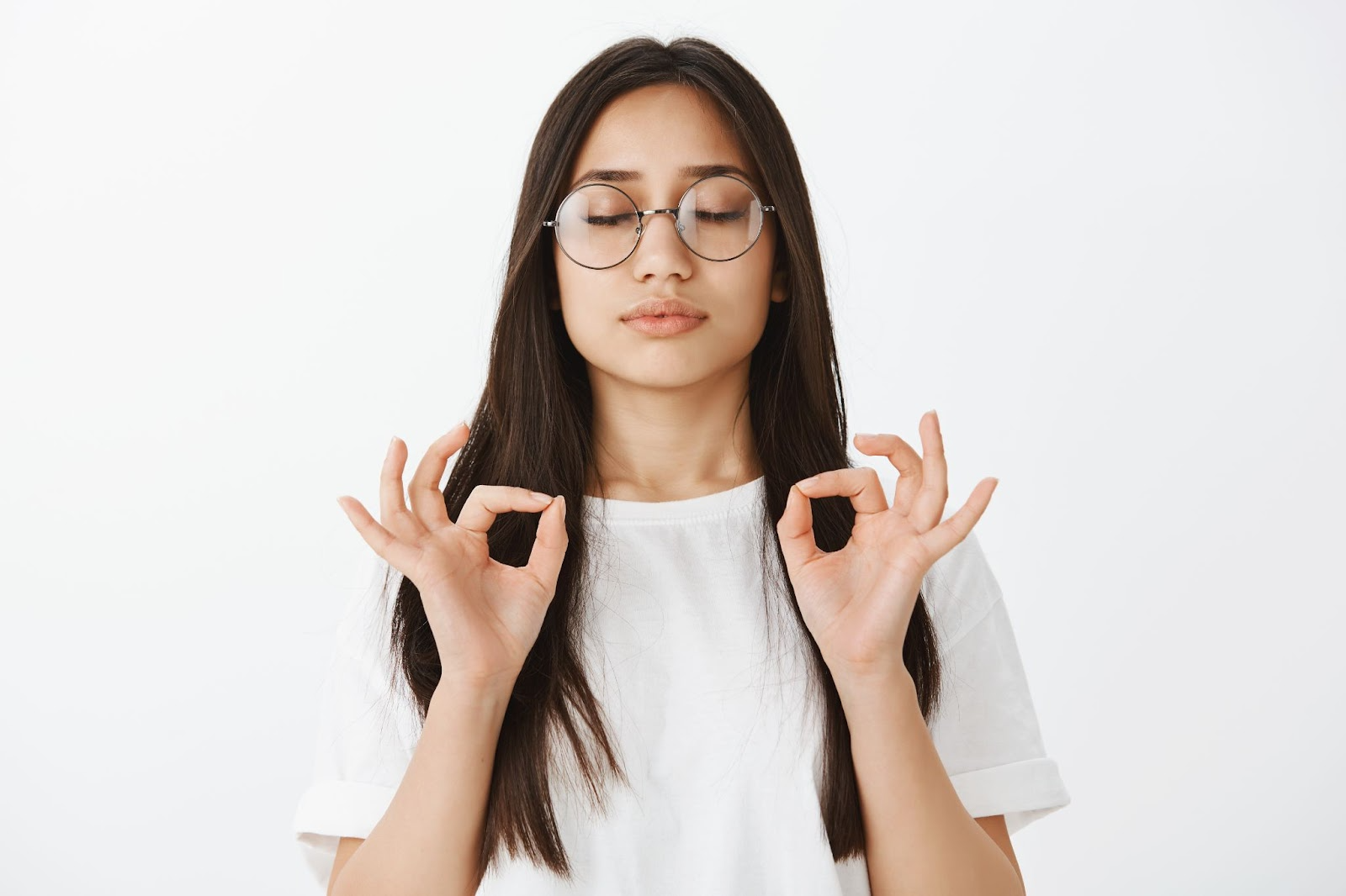 Mujer joven con gafas haciendo gesto de OK con ambas manos y ojos cerrados en señal de aprobación