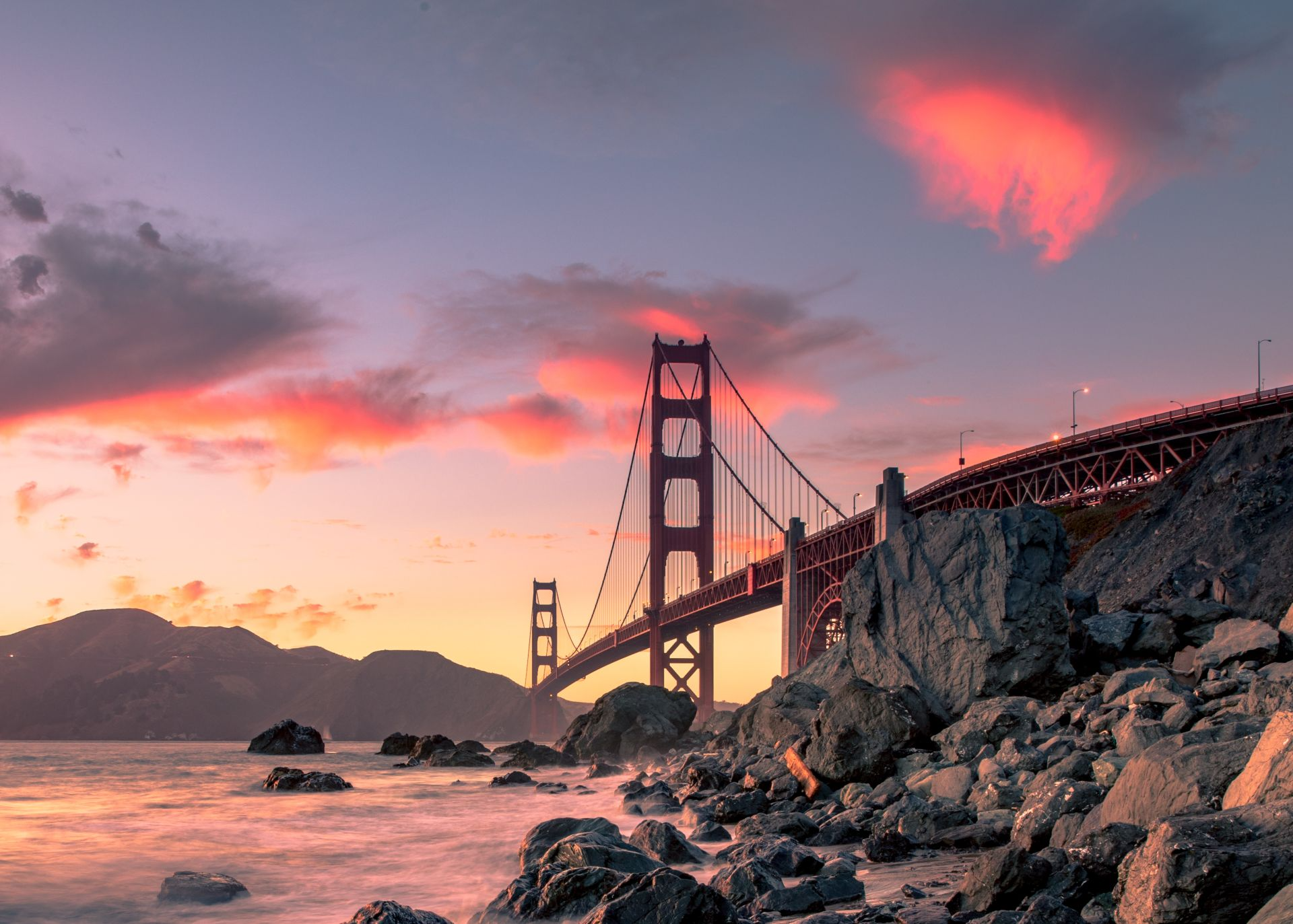 Golden Gate Bridge at dramatic sunset with rocky coastline during west coast road trip