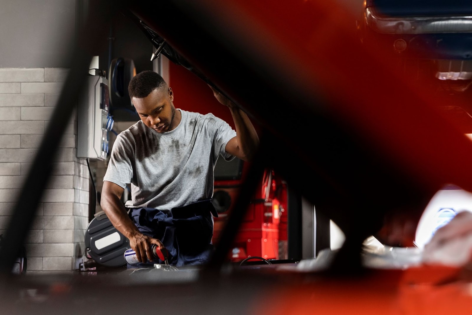 Auto mechanic performing maintenance work on red vehicle in garage