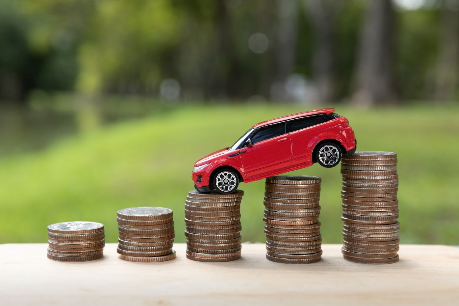 Red toy car climbing stacks of coins representing rising vehicle costs