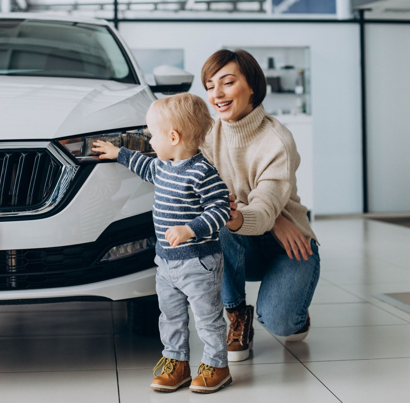 Madre e hijo pequeño explorando SUV blanca nueva en sala de exhibición de concesionaria