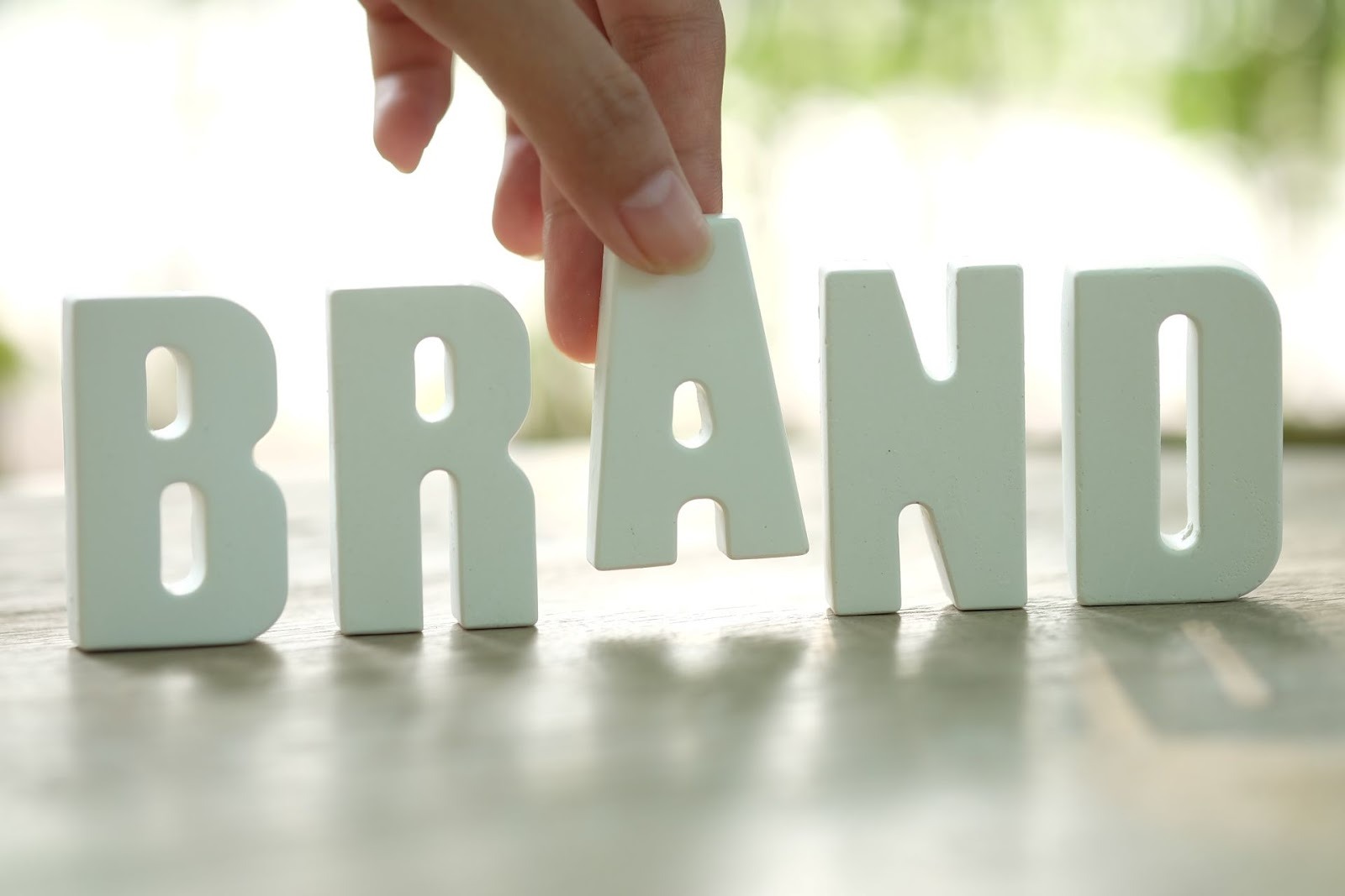 Hand arranging BRAND letters representing monthly car maintenance costs by manufacturer