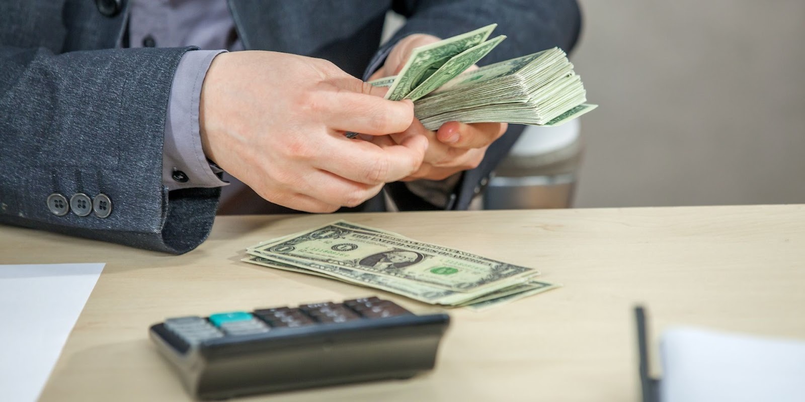 Car dealership salesperson counting cash with calculator to evaluate vehicle trade-in value