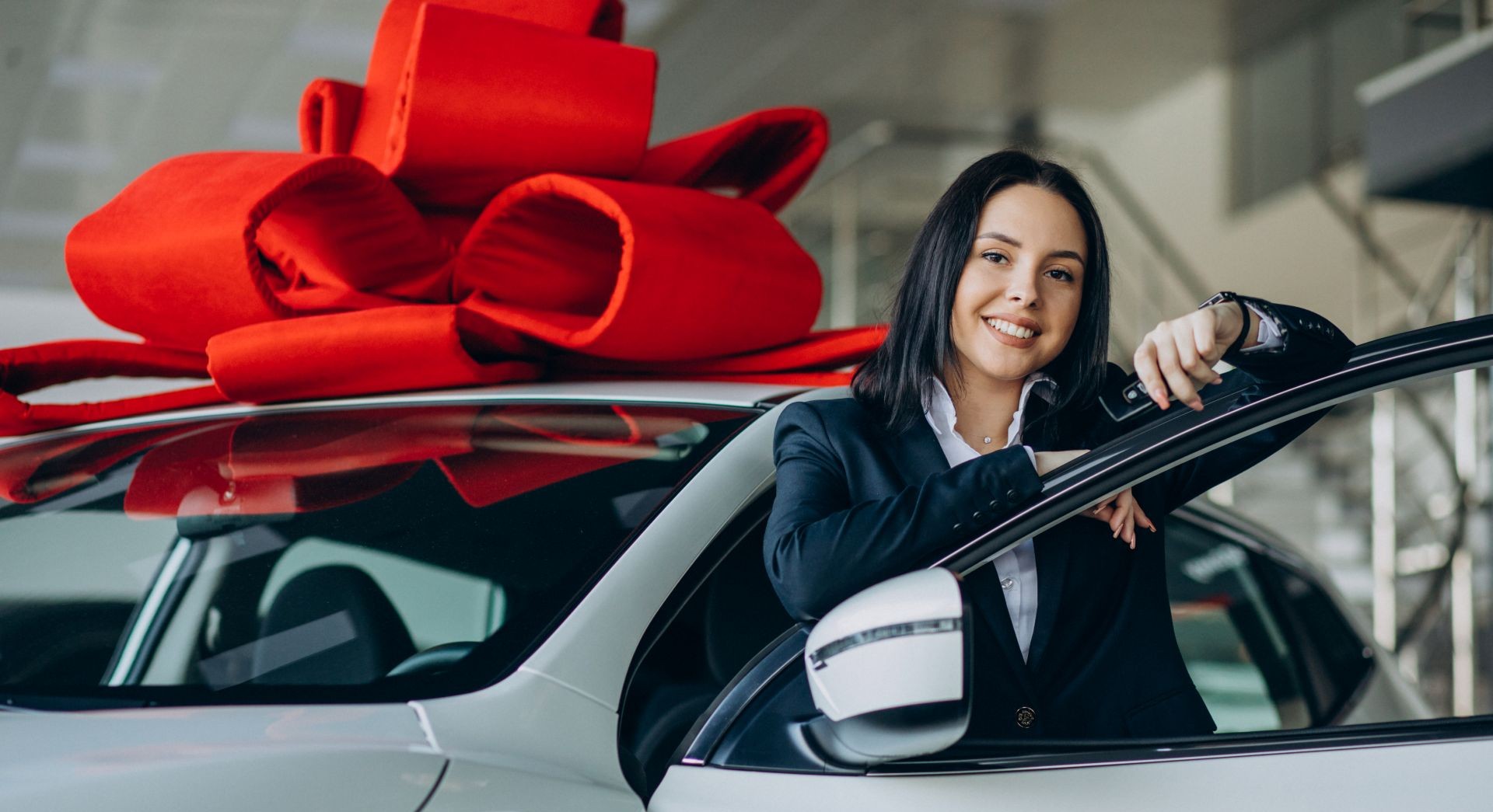 Happy customer receives her first new car with red bow at dealership