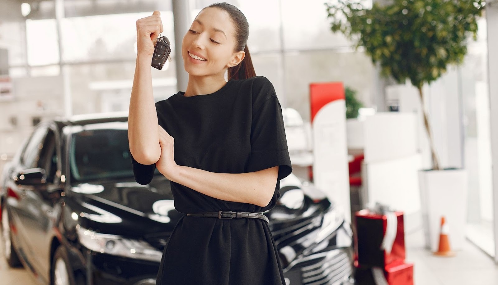 Excited woman holds keys to her new car at dealership after successful vehicle purchase