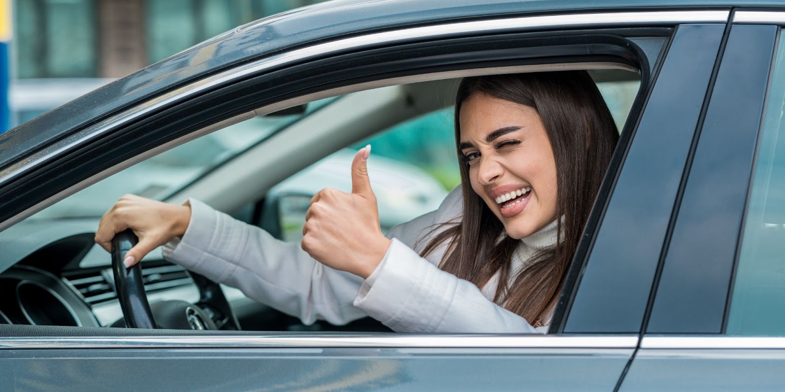 Mujer conductora feliz haciendo señal de pulgar arriba desde la ventana de su auto nuevo