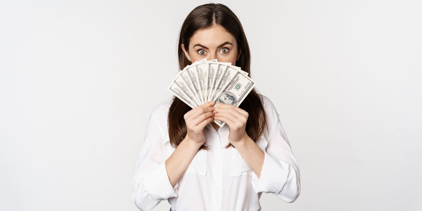 Mujer joven sorprendida sosteniendo billetes de dólares americanos en abanico preparada para realizar su pago