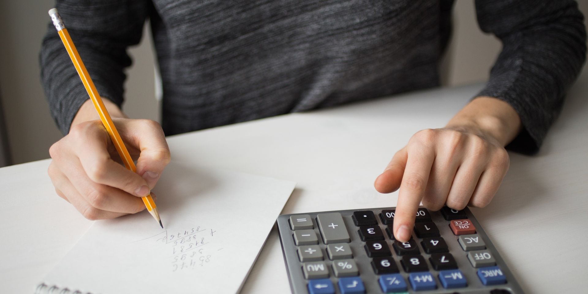 Persona calculando registration fee con calculadora y anotando números en papel con lápiz