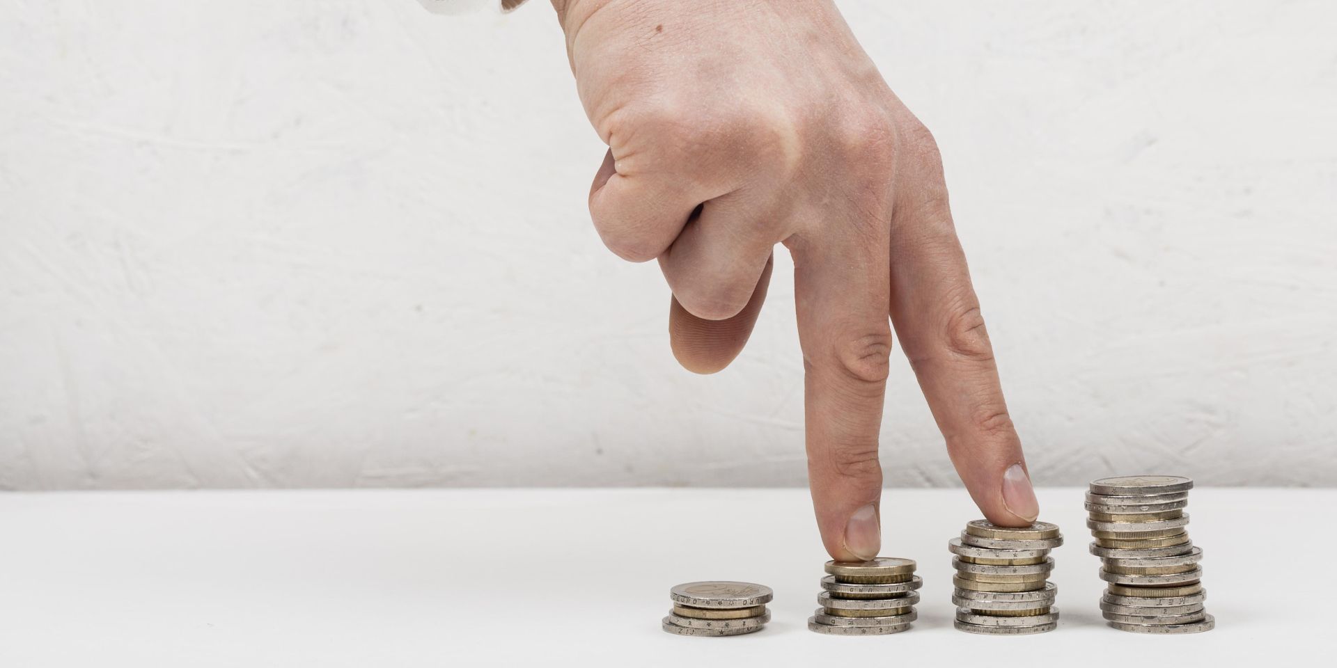 Mano caminando sobre pilas de monedas en crecimiento representando ahorro e inversión progresiva