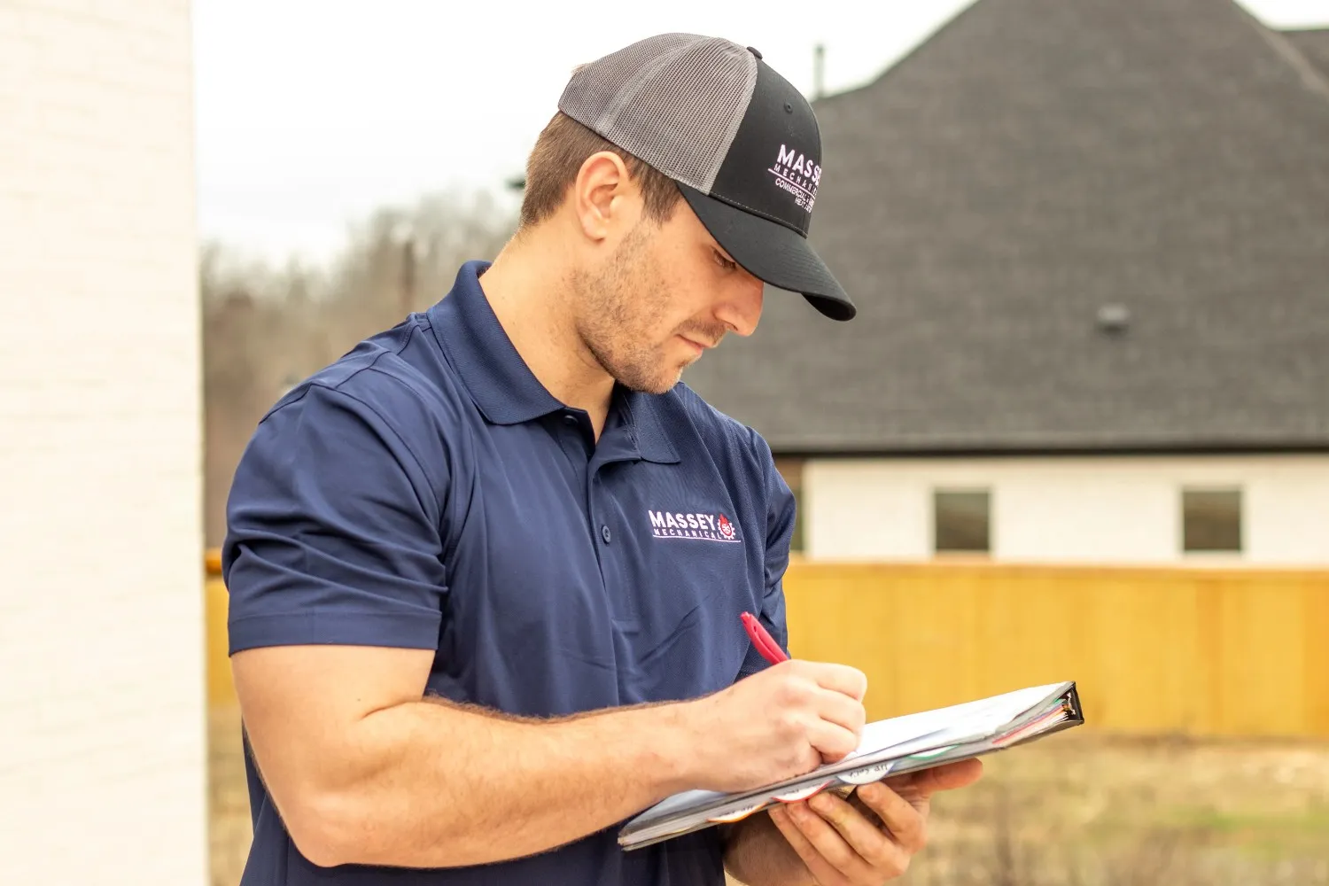 A man in a baseball cap writes on a clipboard, focused on his task.