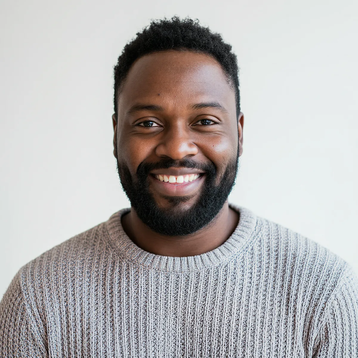 Smiling bearded man wearing a gray knit sweater against a light background.