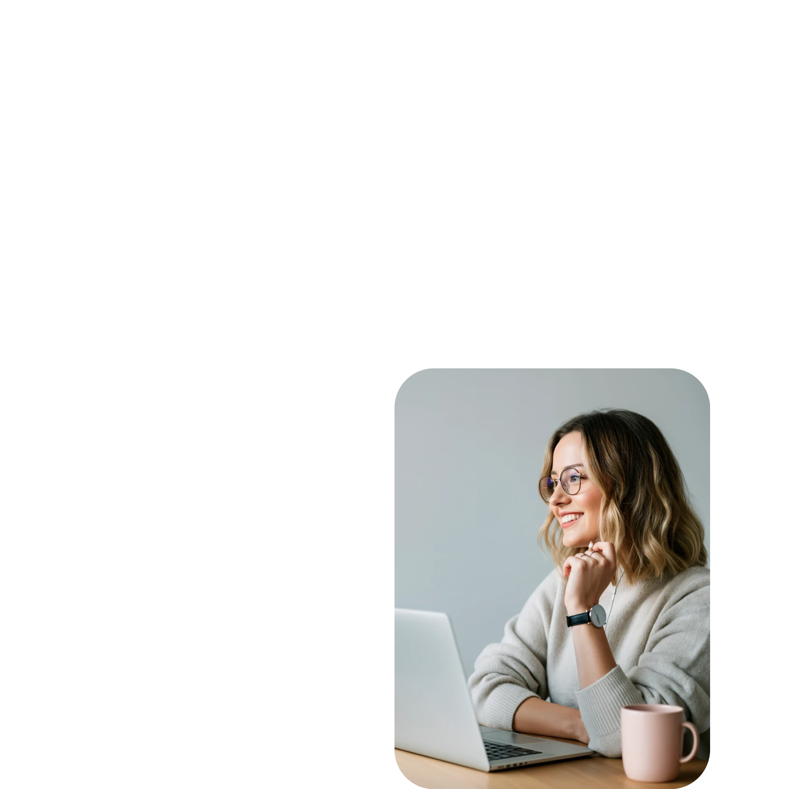 Smiling woman with glasses working on a laptop at a desk with a pink mug.