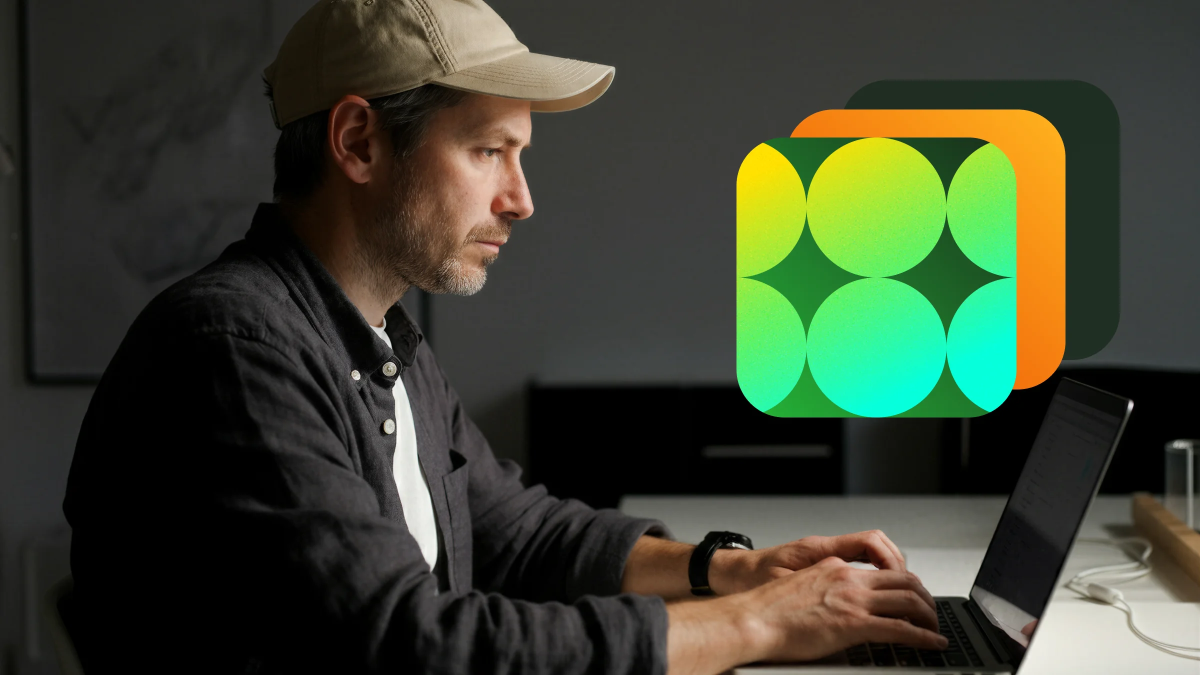 Man wearing a beige cap and black shirt typing on a laptop at a desk with a green and orange abstract graphic overlay.