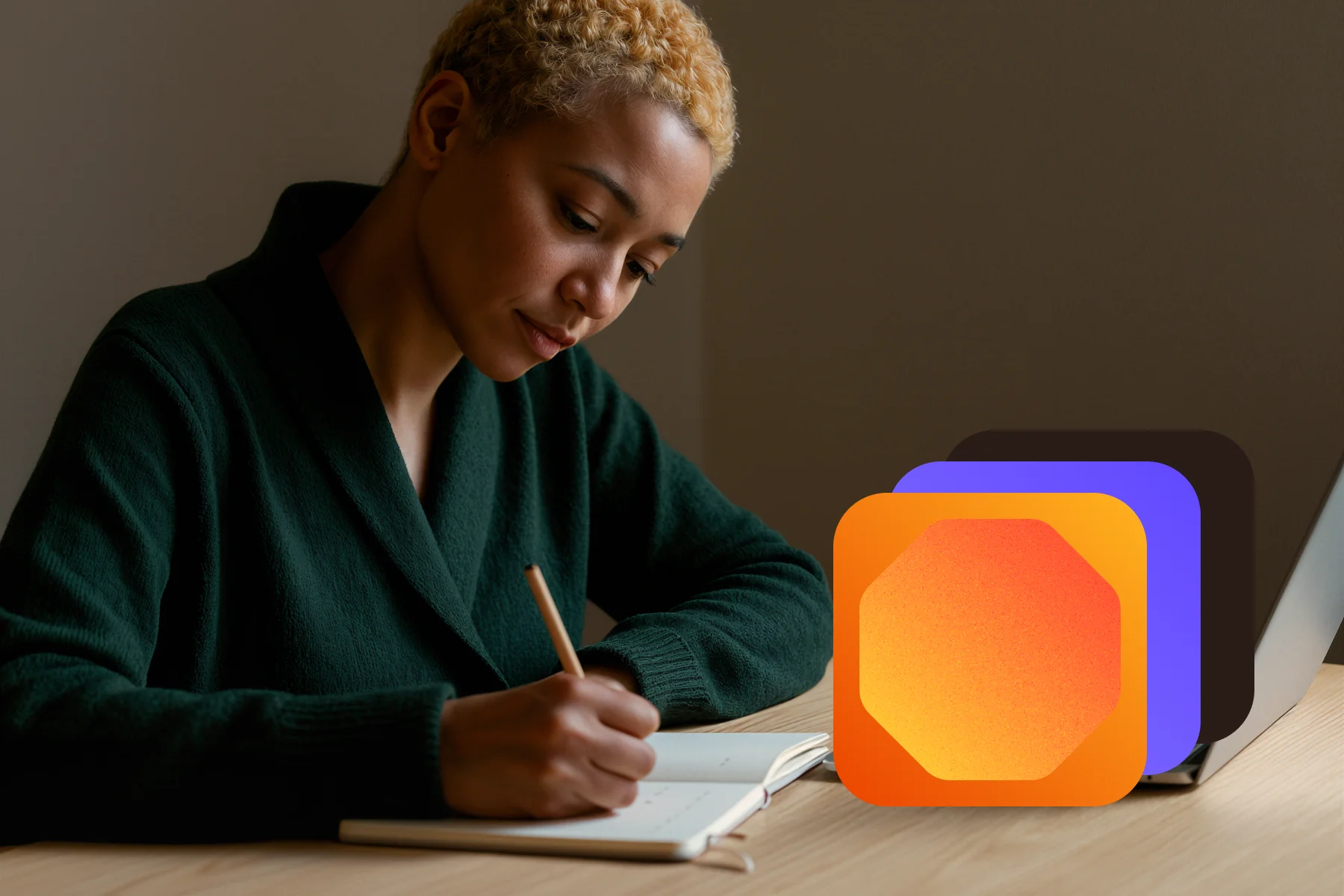 Person with short curly hair writing in a notebook at a desk with a laptop and colorful abstract shapes.
