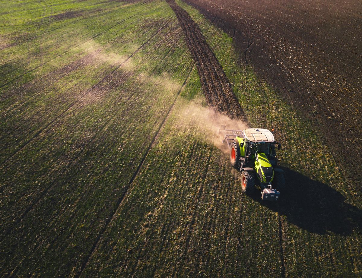 Aerial view of a tractor working a cultivated field, raising dust