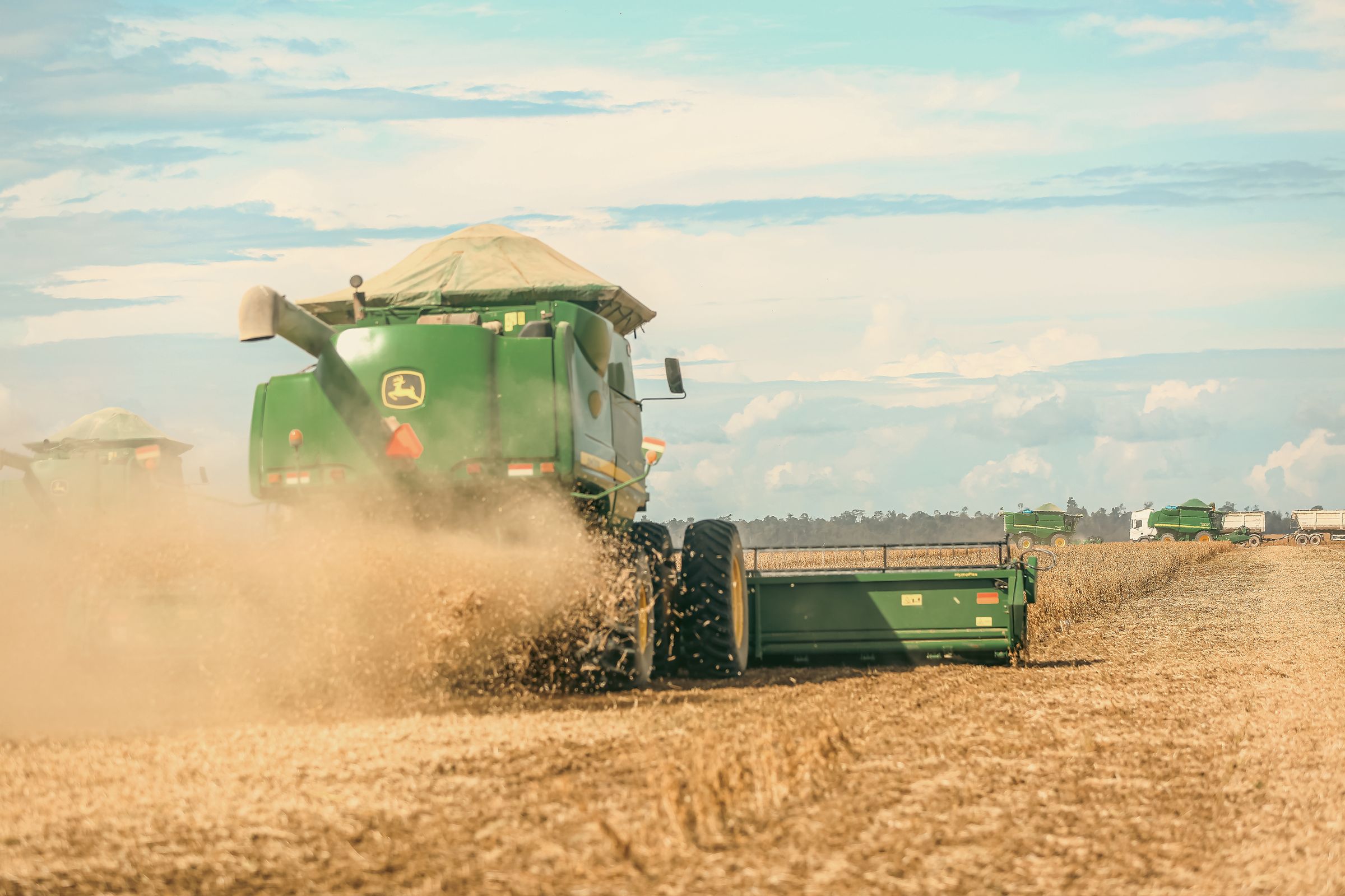 A combine harvester throws up dust as it harvests a dry soybean field under a hot sky in Brazil