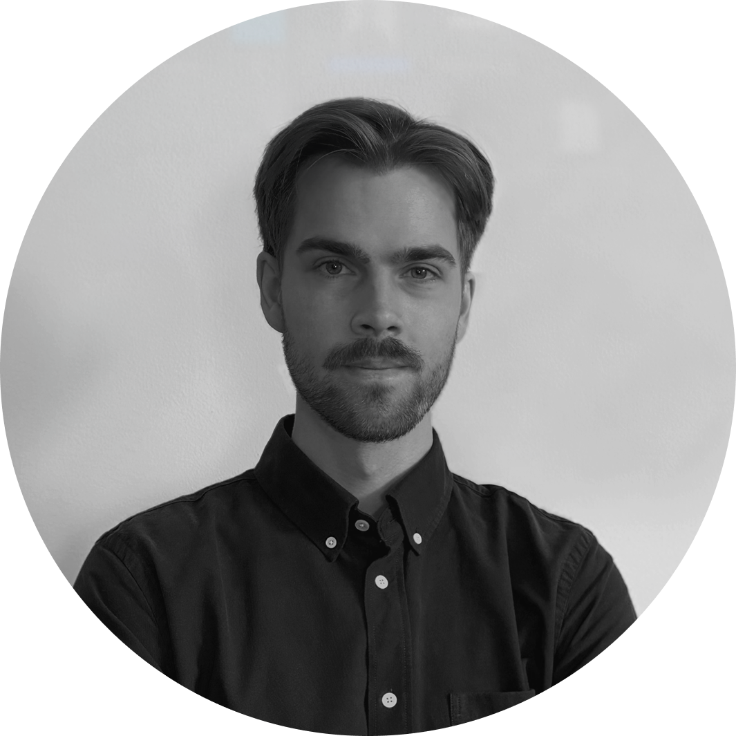 Black and white portrait of a young man with short hair and a beard wearing a dark button-up shirt.