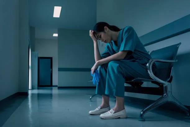 Nurse sitting tired in hospital hallway showing signs of burnout