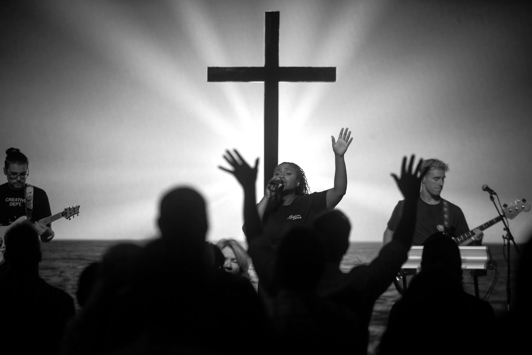 Worship under a backlit cross, hands raised across the room