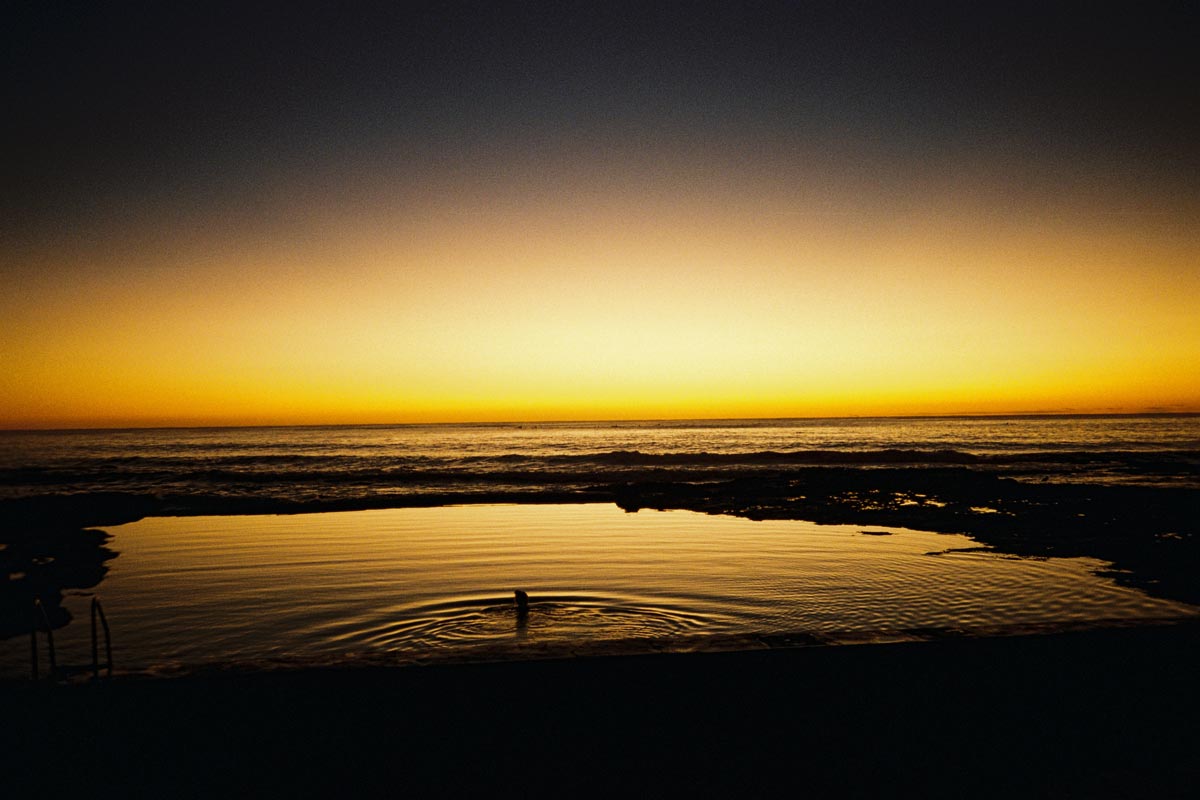 An image of a sunset, over the ocean. There is a pool of water in the foreground.
