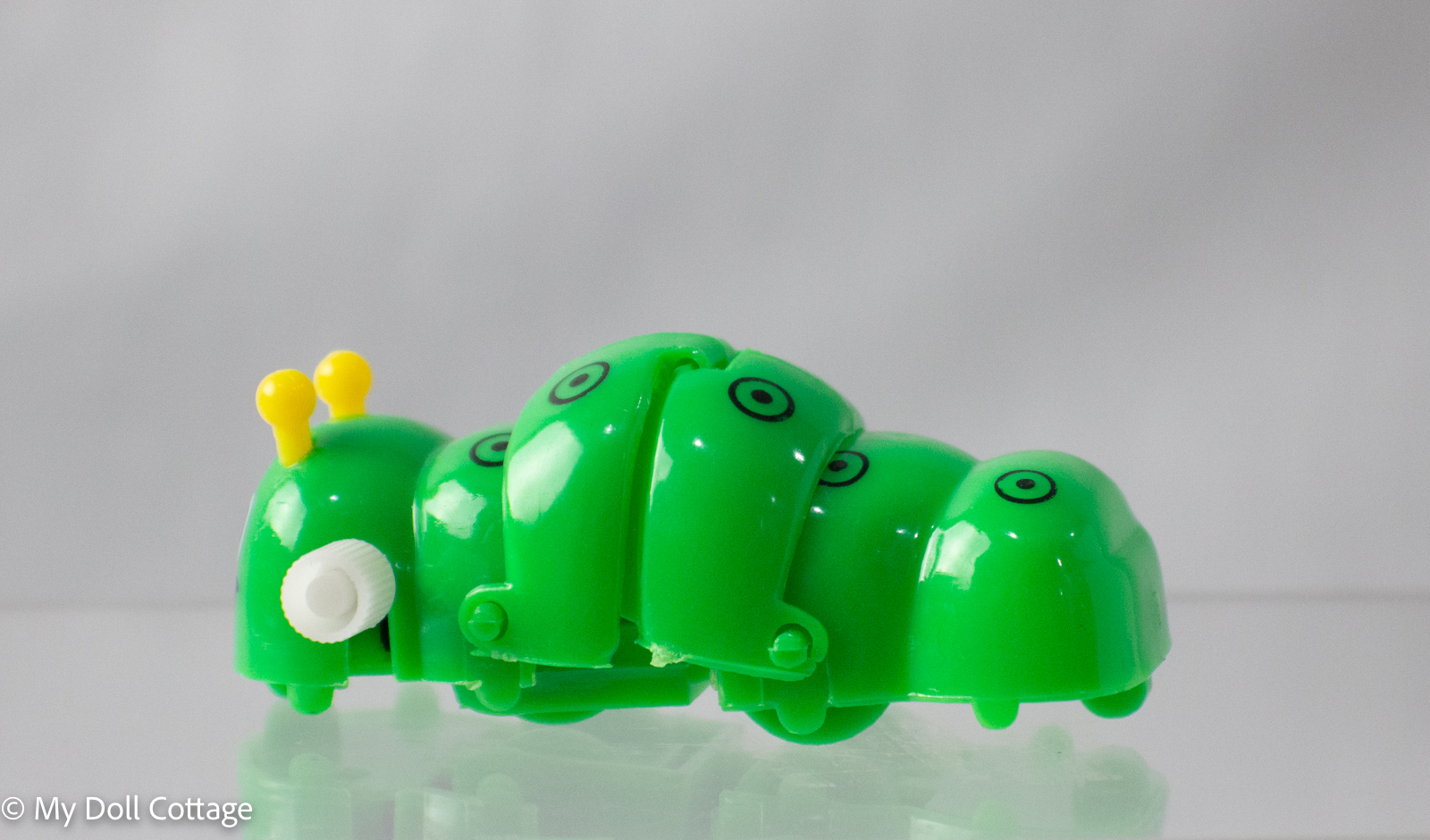 Side view of the vintage wind-up green caterpillar toy No. 3938, showing segmented body and yellow antenna on face.