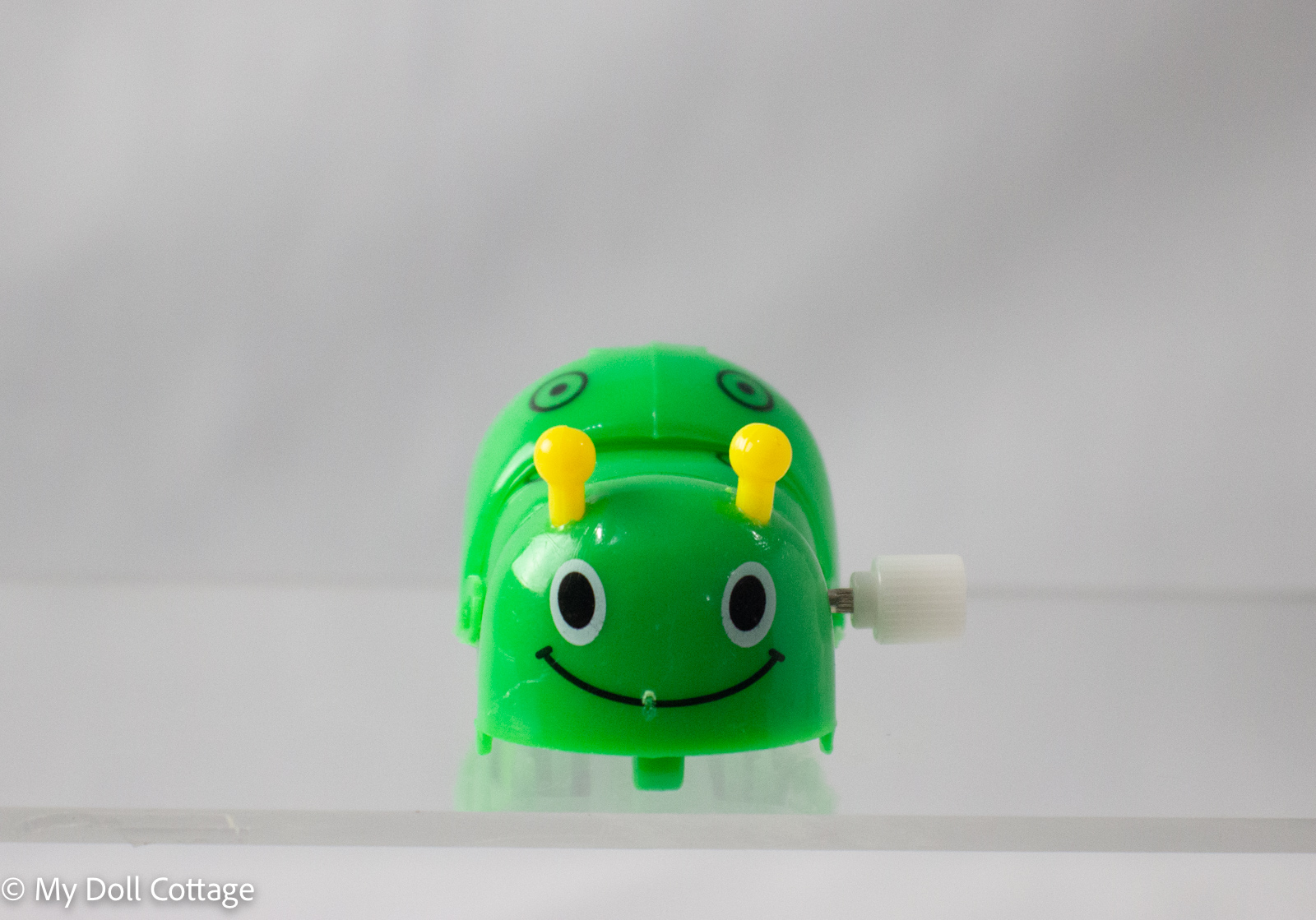 Front view of the wind-up green caterpillar, smiling face visible with wind-up key on side.