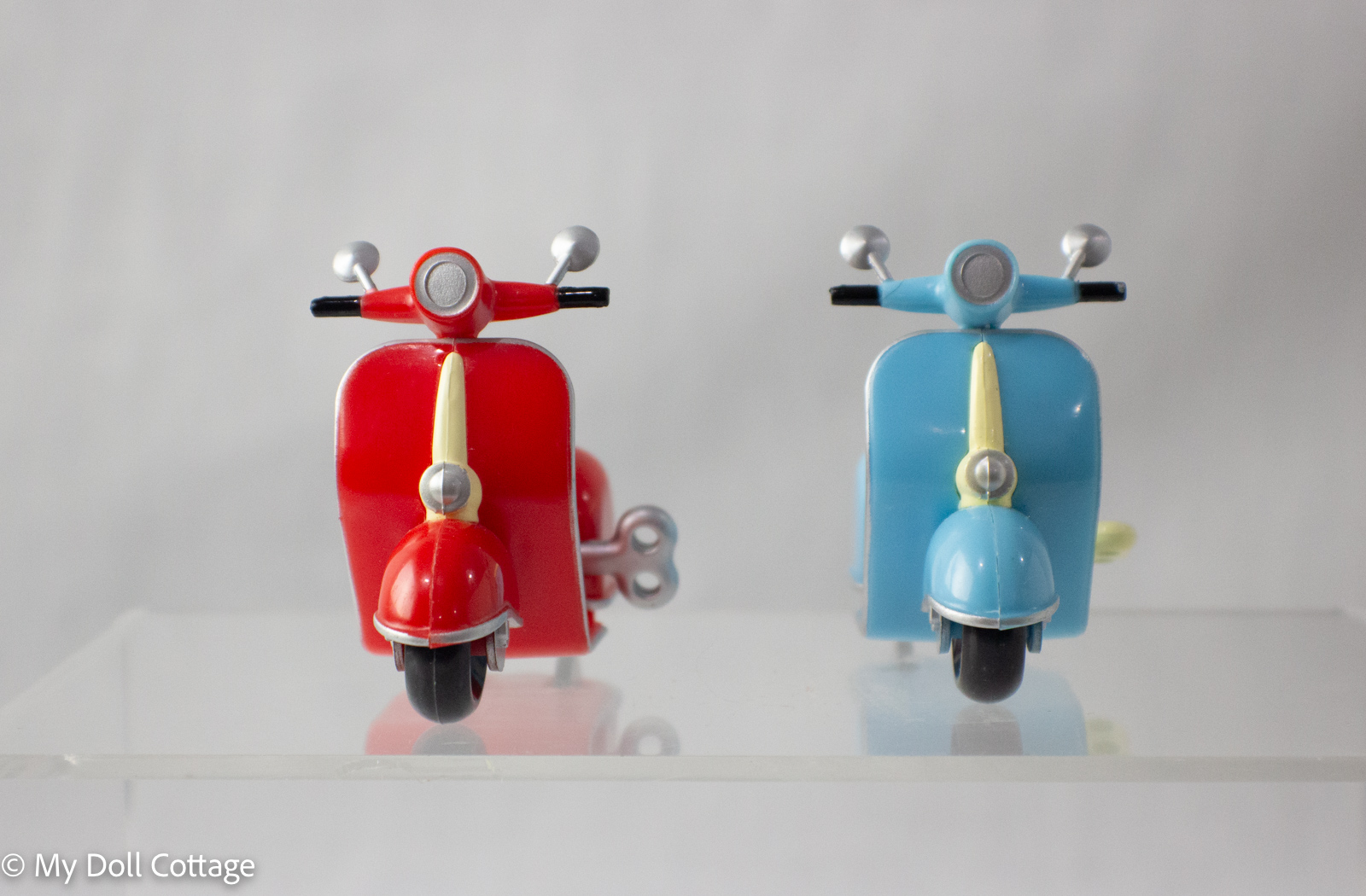 Front view of two 1980s Chinese wind-up mopeds, one red and cream, one blue and cream.