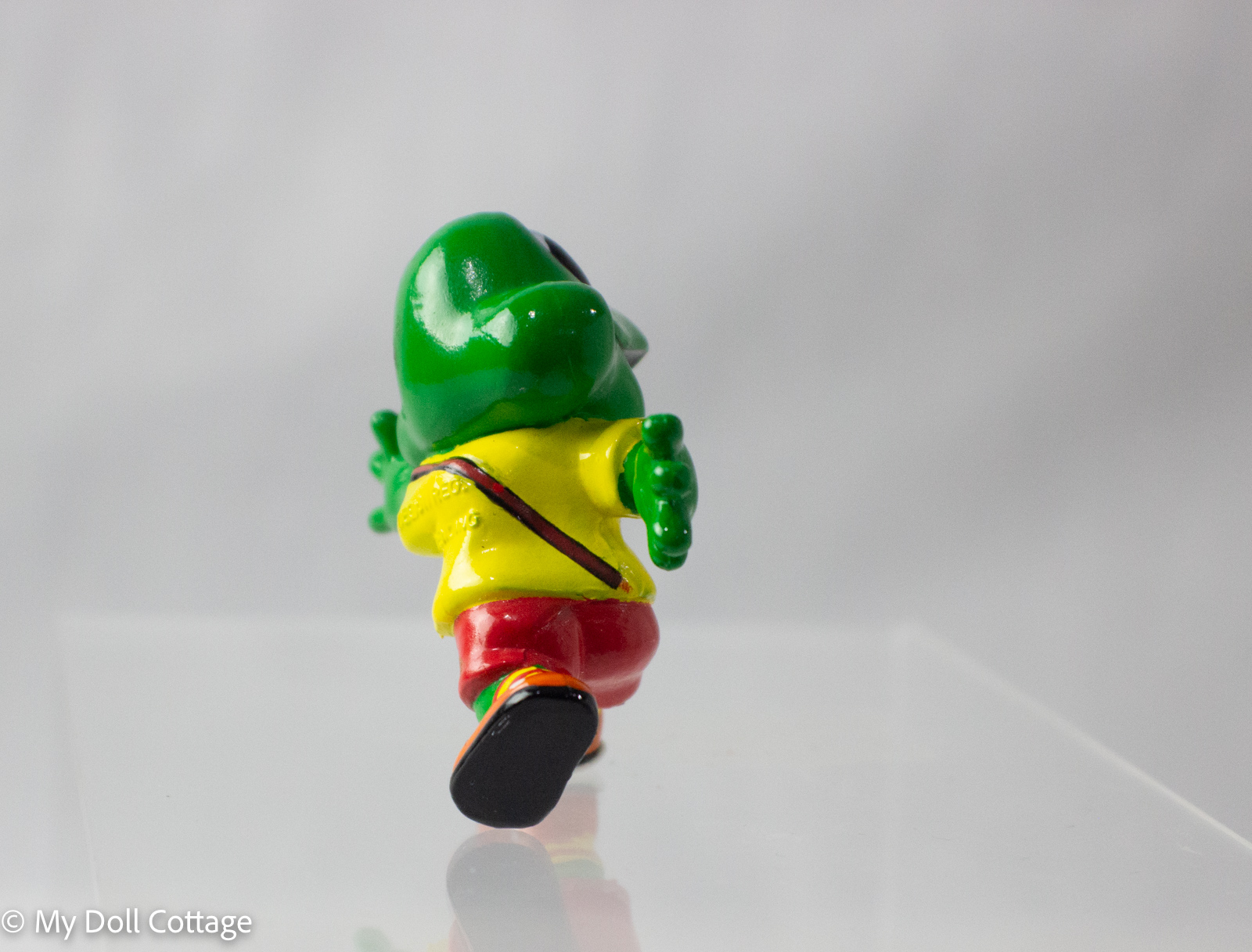 Back angle of Freddo Frog figurine running with football, highlighting striped socks and bright orange shoes.