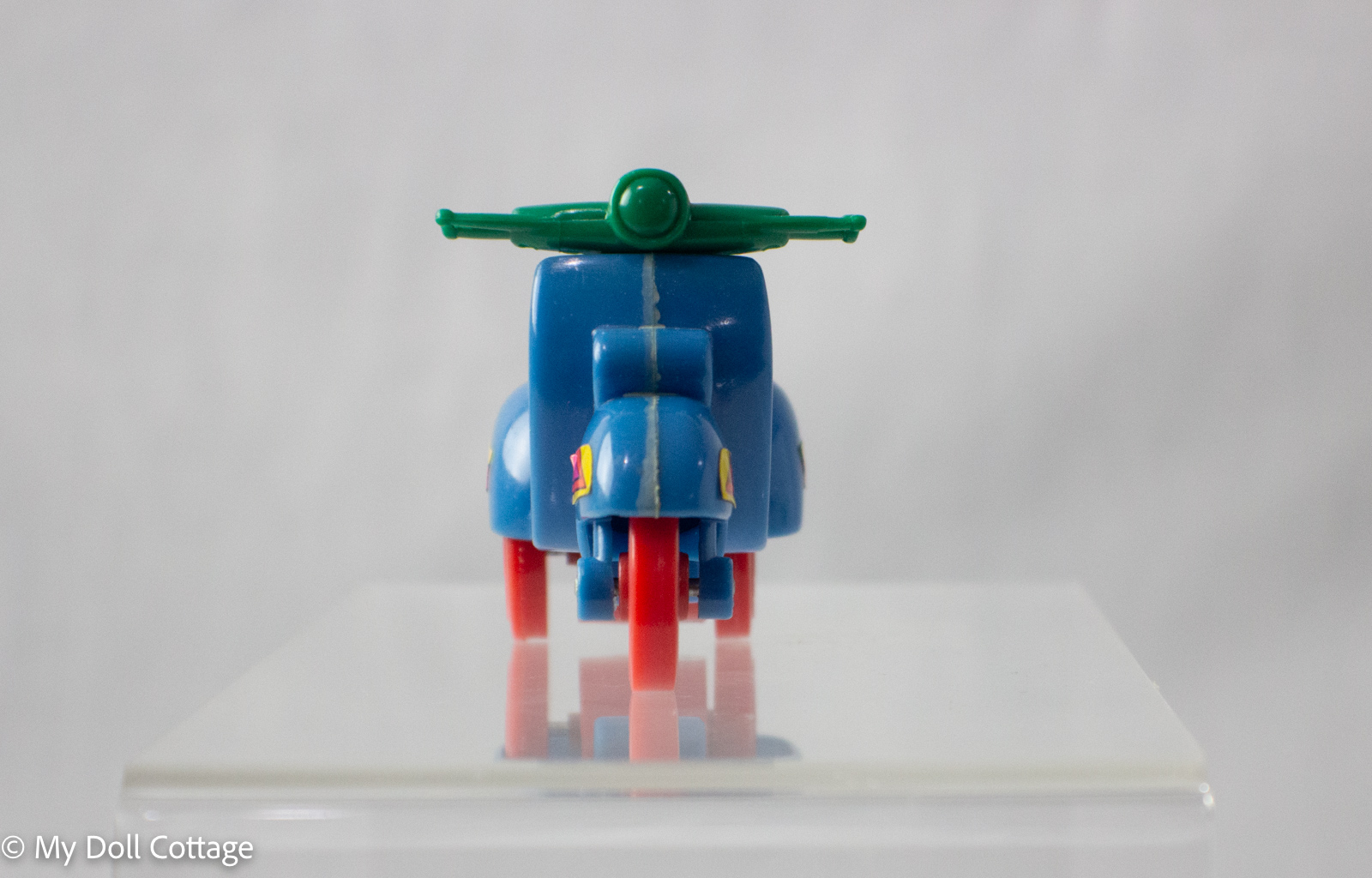Front view of blue scooter pencil sharpener with green handlebars and red wheels.