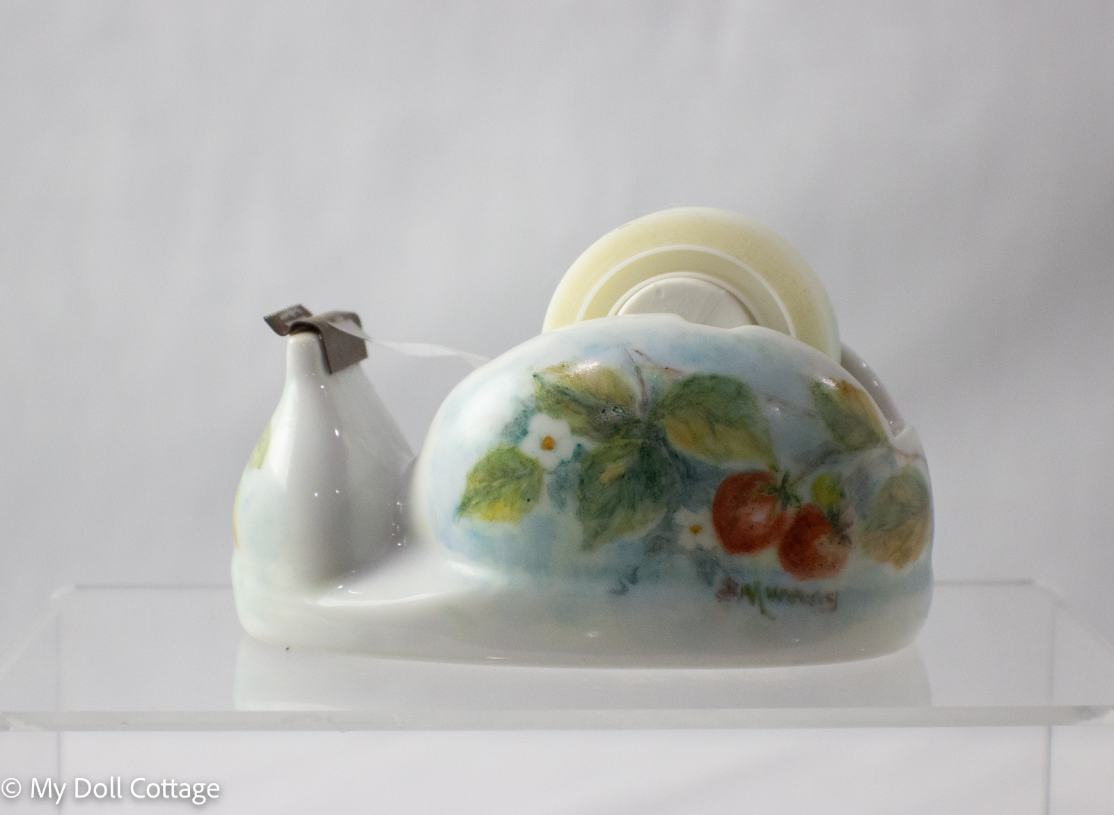 Side view of ceramic strawberry sticky tape holder with strawberries and leaves painted on surface.