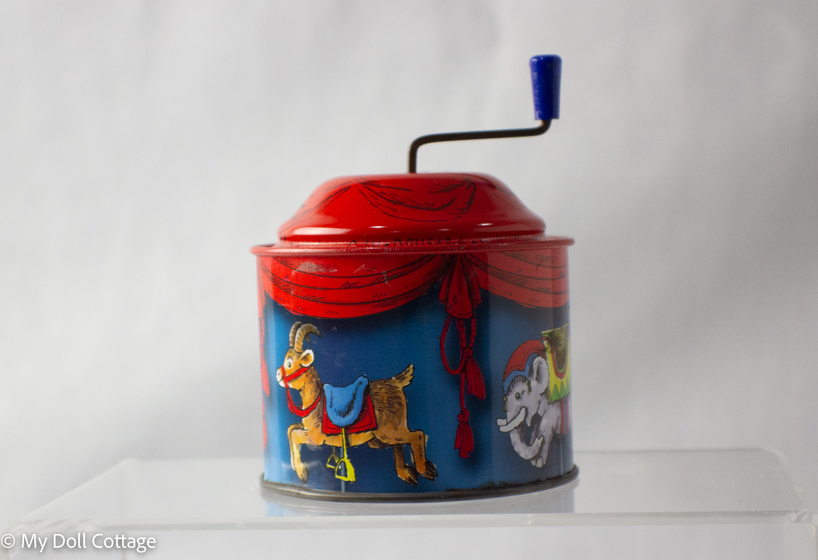 Angled view of the carousel chime toy showing goat and elephant details and blue crank handle.