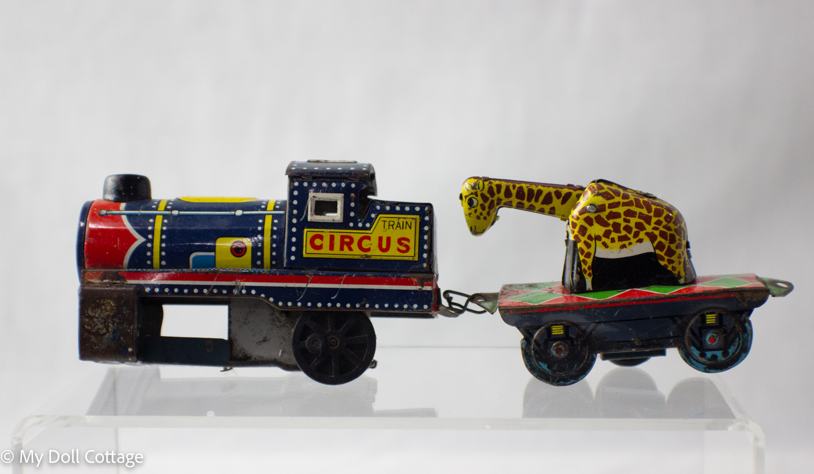 Side view of vintage 1950s lithographed tin circus train with blue and red engine marked 'CIRCUS TRAIN' pulling three colourful carriages.