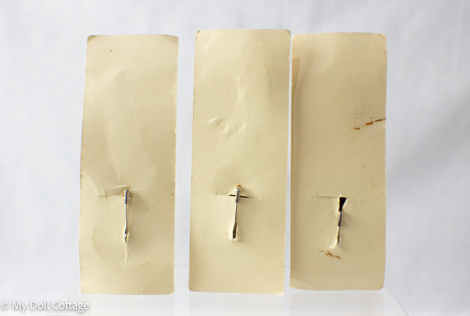 – Rear view showing simple metal pin clasps on cream backing cards with minor age wear.
