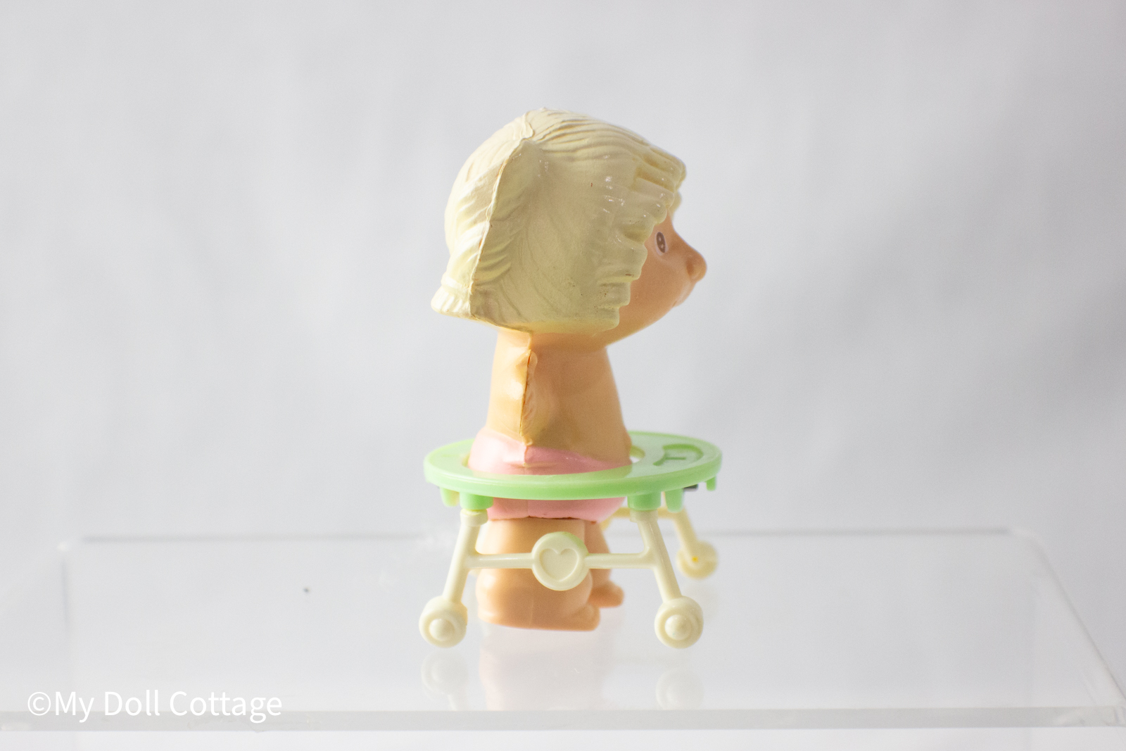 A blonde Cabbage Patch Kid wind-up baby toy in a pastel green walker, wearing a pink diaper, made by Tomy in 1983.