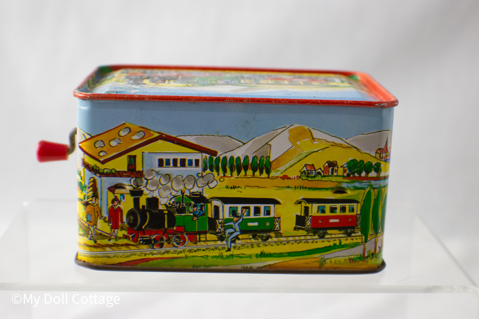 - Opposite side view featuring red and green train leaving a countryside station.