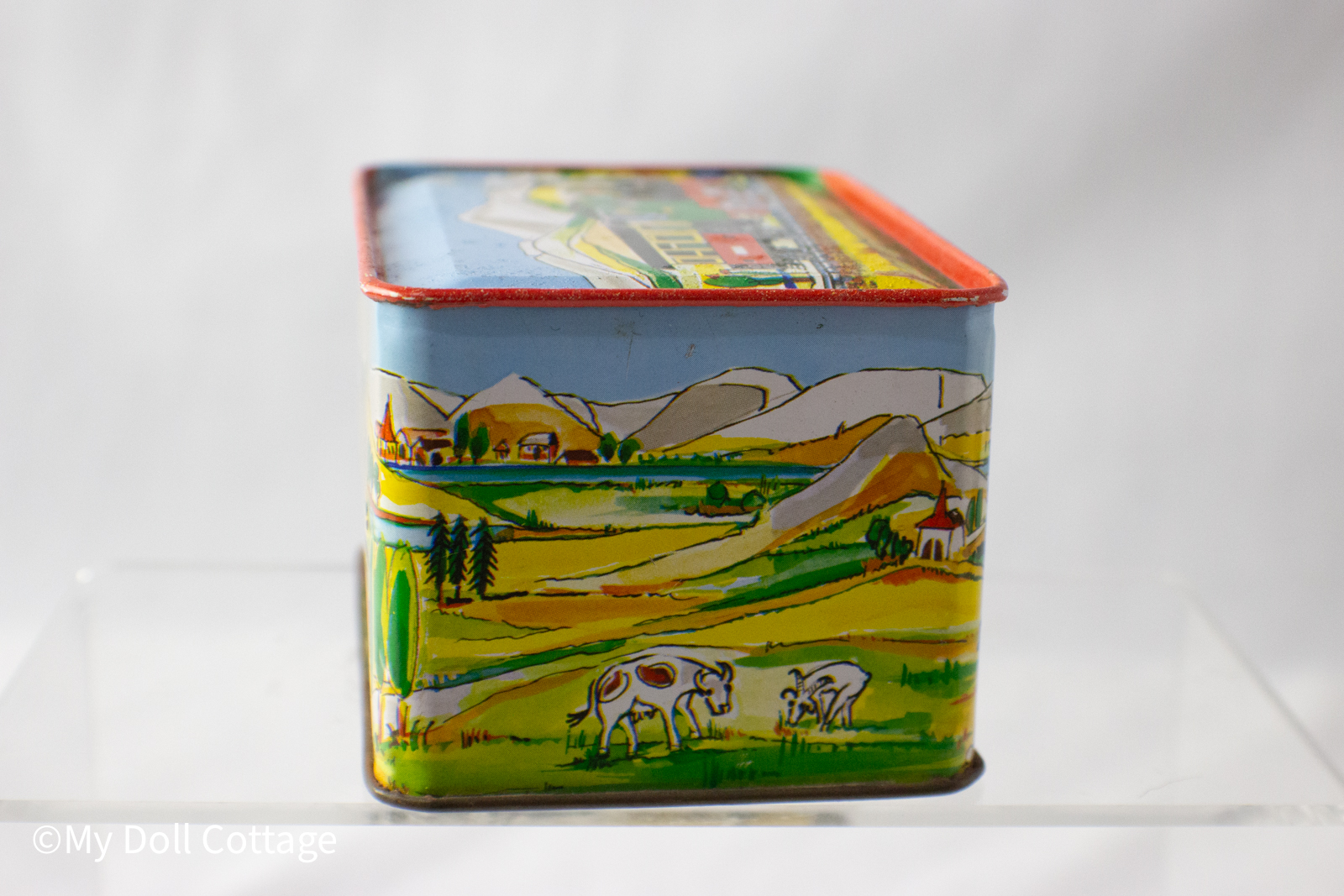 - Side view of lithographed tin music box with train crossing bridge over river and mountain scenery.