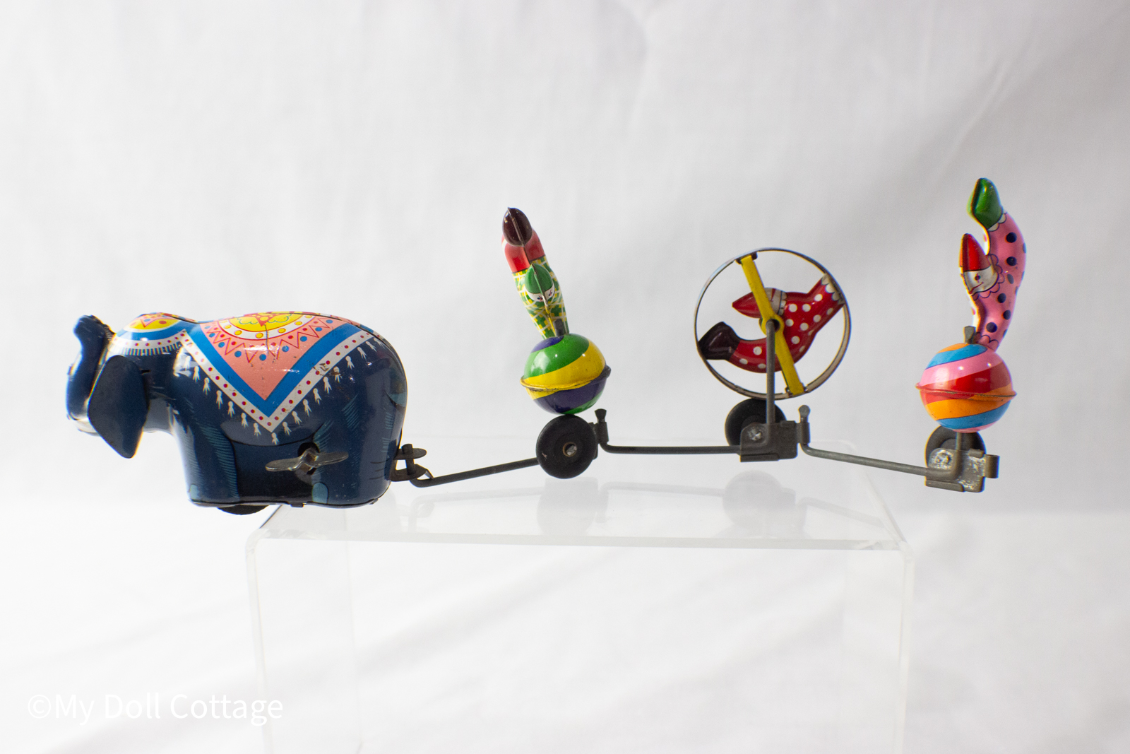 Side view of 1950s TPS lithographed tin circus toy showing blue elephant pulling three colourful acrobats on wheels.